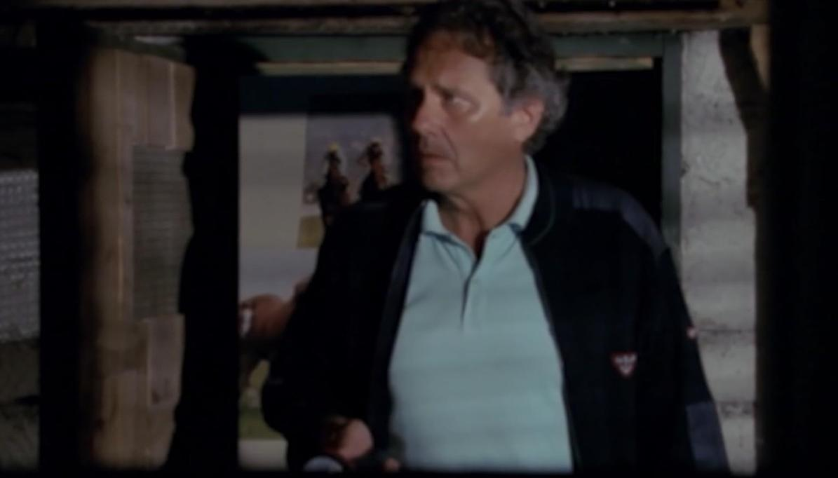 Ein Mann mittleren Alters mit grauem Haar trägt ein hellblaues Poloshirt und eine dunkle Jacke.