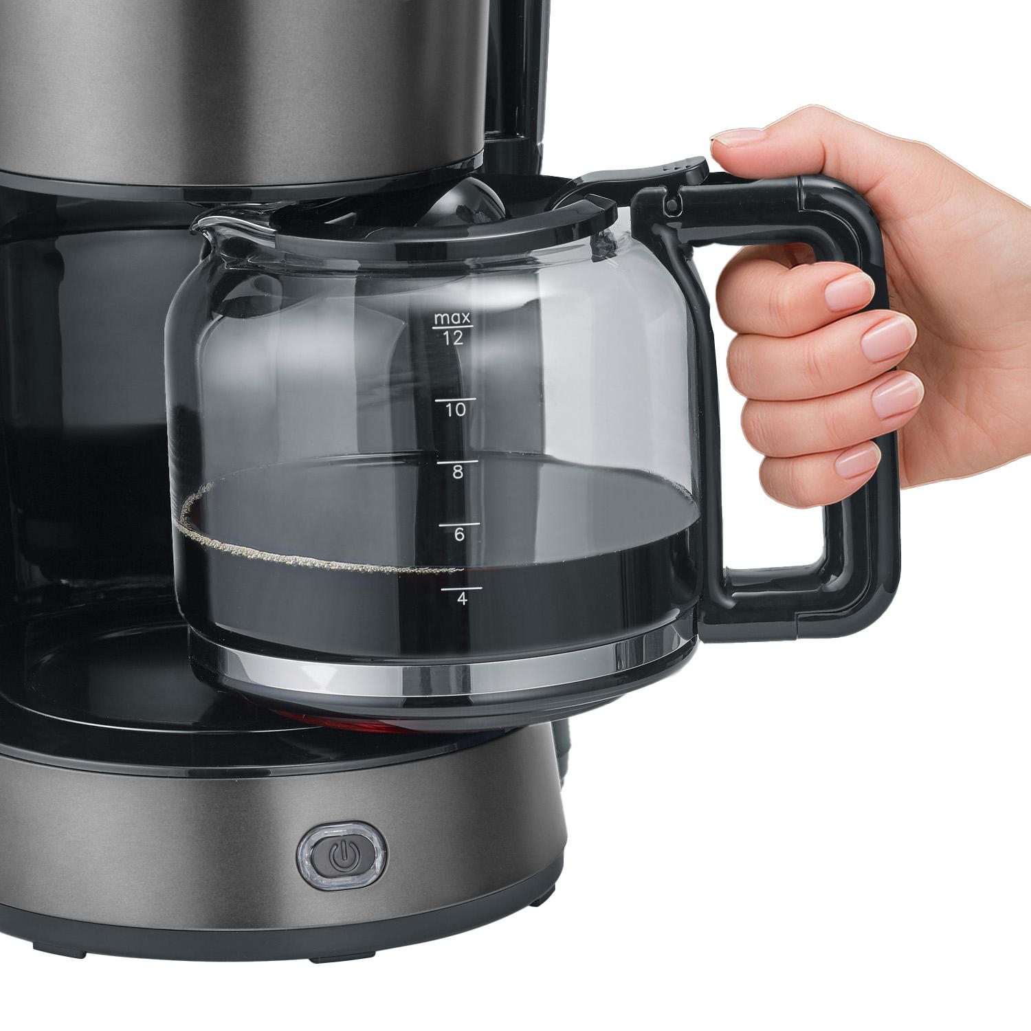 Eine Hand hält den Griff einer Kaffeekanne aus Glas mit Kaffee.