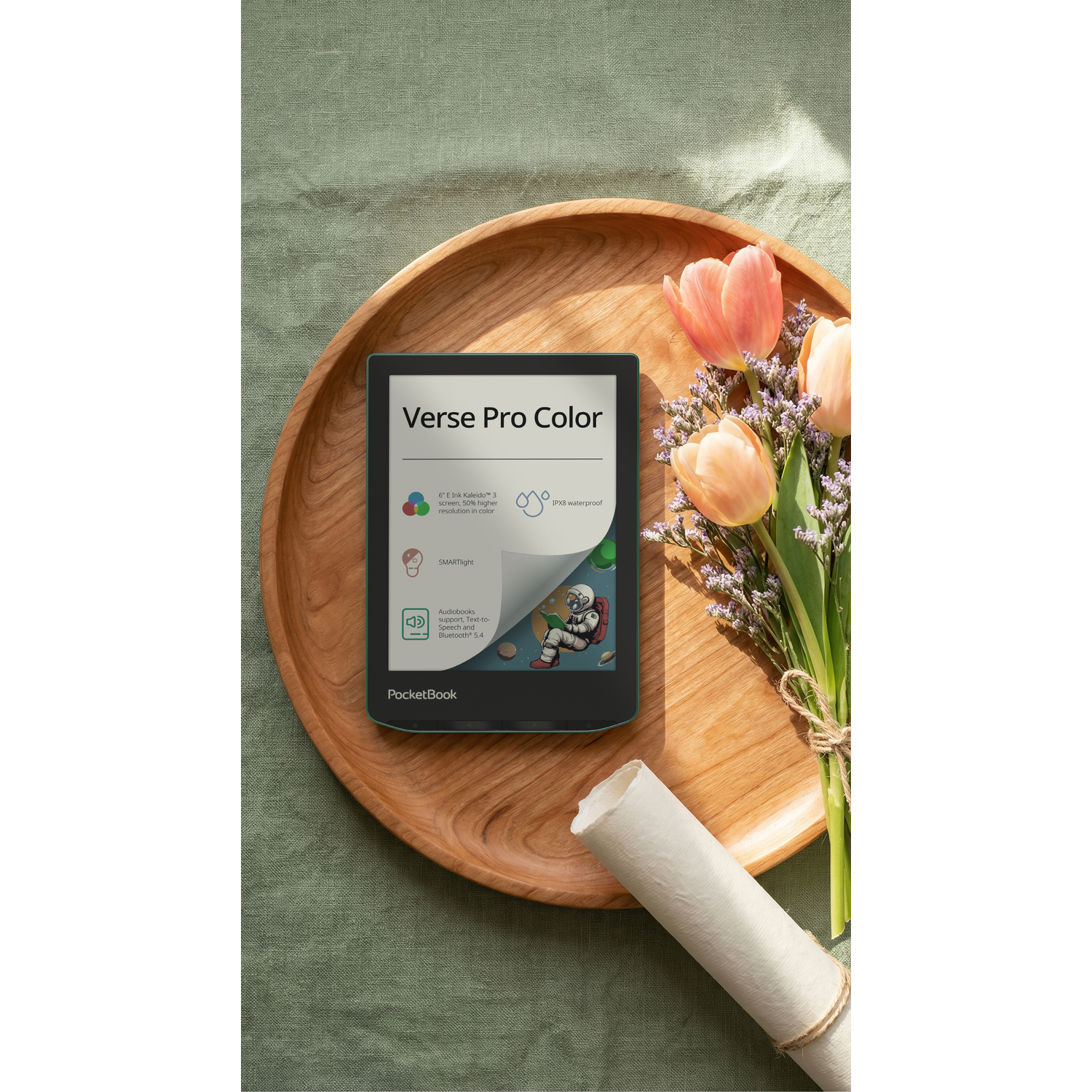 Een e-reader met kleurenscherm ligt op een houten schaal naast tulpen en een rol.