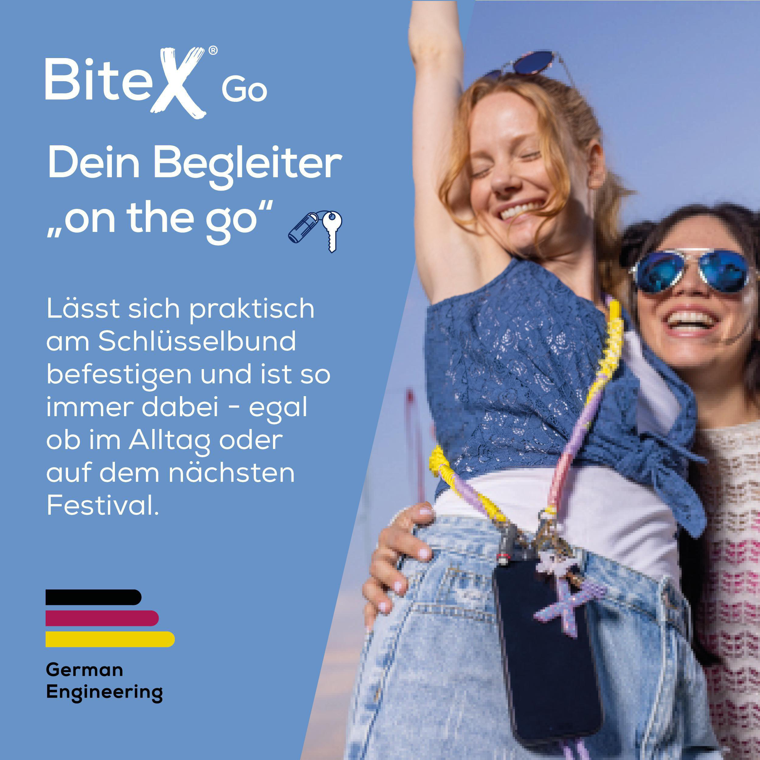 Zwei lachende Frauen mit einem Smartphone am Schlüsselbund, blauer Himmel.