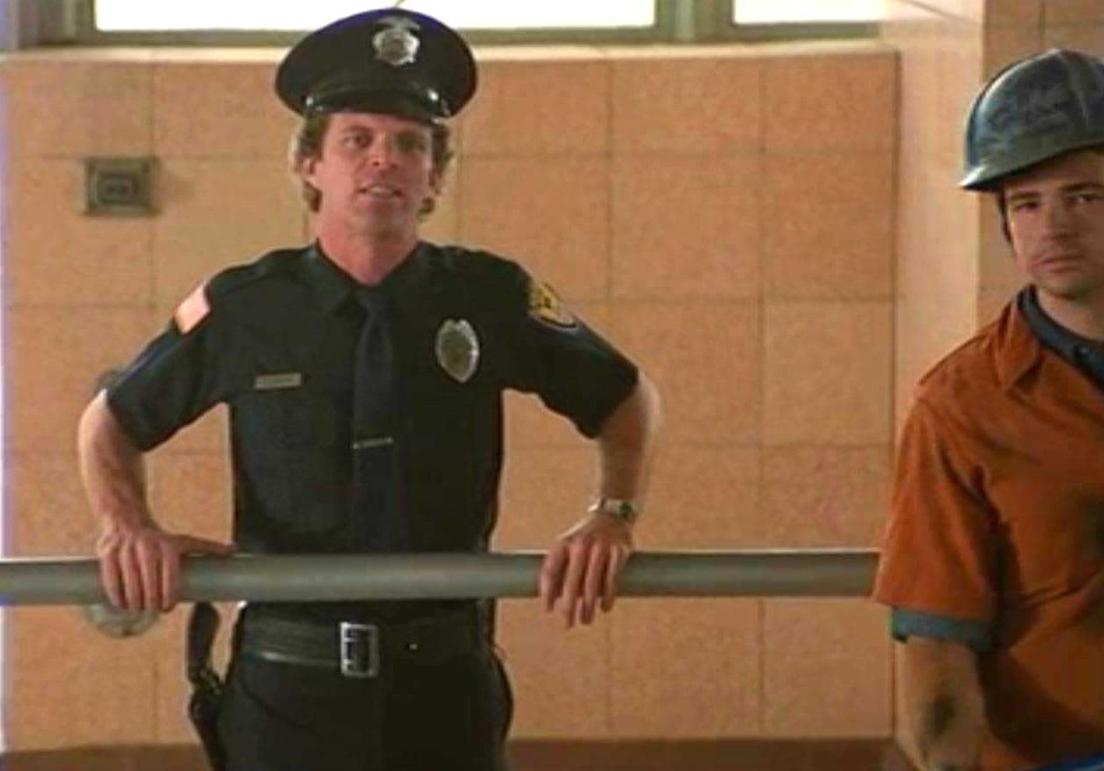 Ein Polizist in Uniform steht neben einem Mann in einem orangefarbenen Hemd.