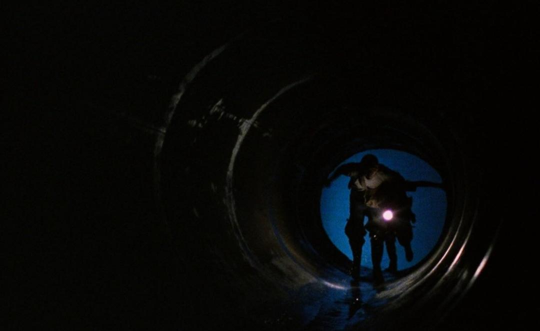 Zwei Personen mit Taschenlampe in einem dunklen, runden Tunnel.