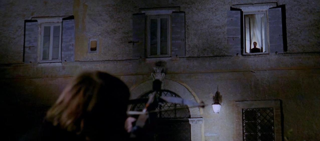 Mann im Fenster einer Hausfassade, im Vordergrund unscharfe Person.