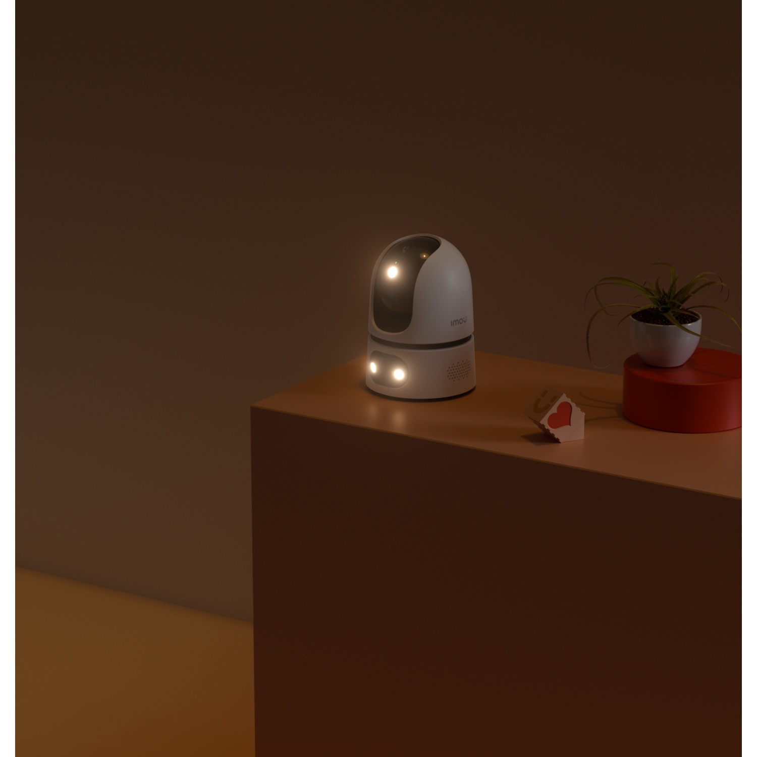 Une caméra Imou blanche est posée sur une table avec une petite plante et un objet rouge.