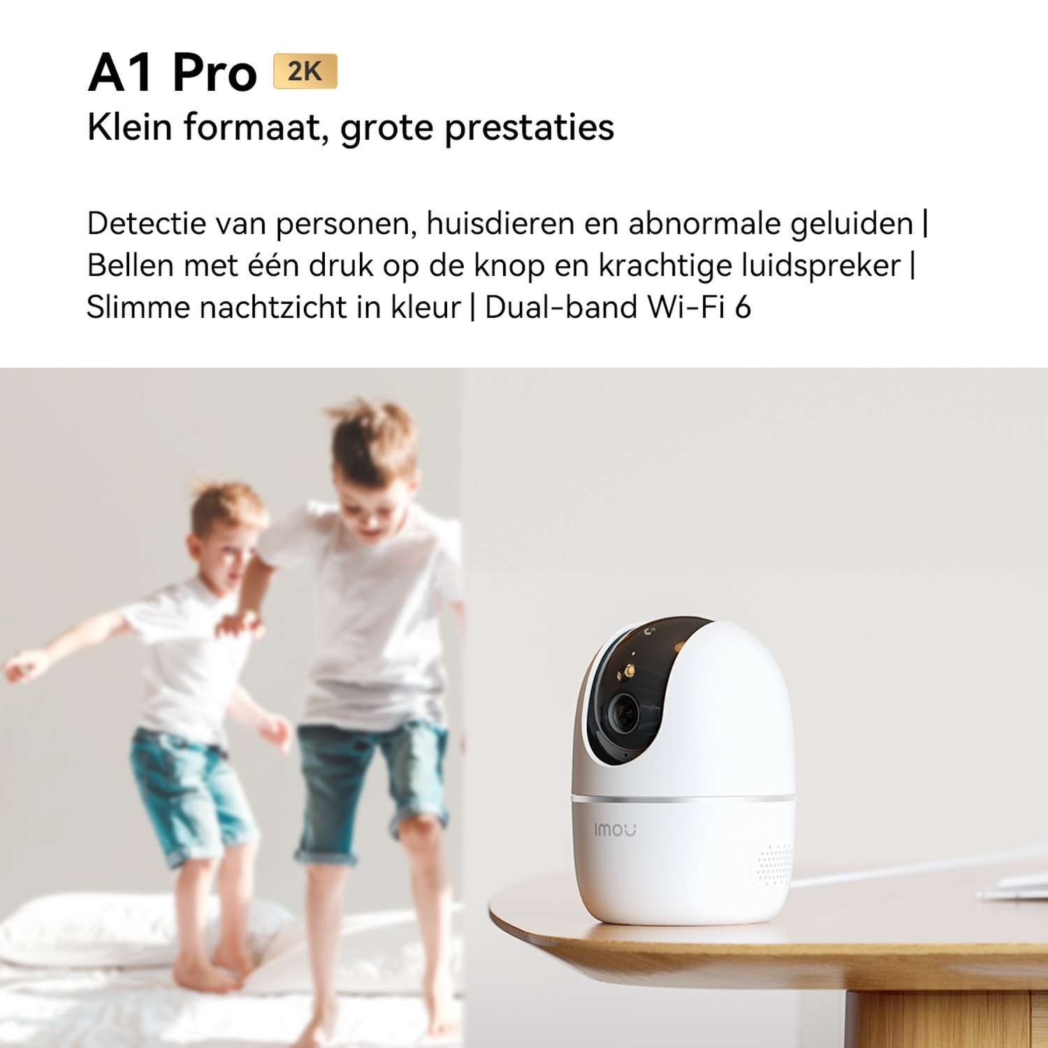 Une caméra de sécurité blanche est posée sur une table en bois. Au fond, deux enfants sautent sur un lit.