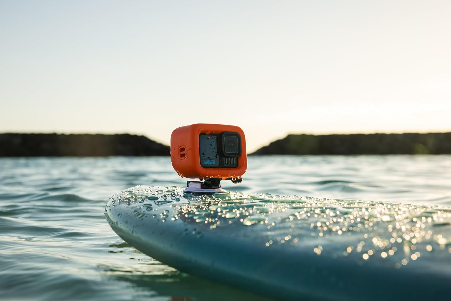 Narancssárga GoPro kamera kék szörfdeszkán vízen, napfénycsillogással.