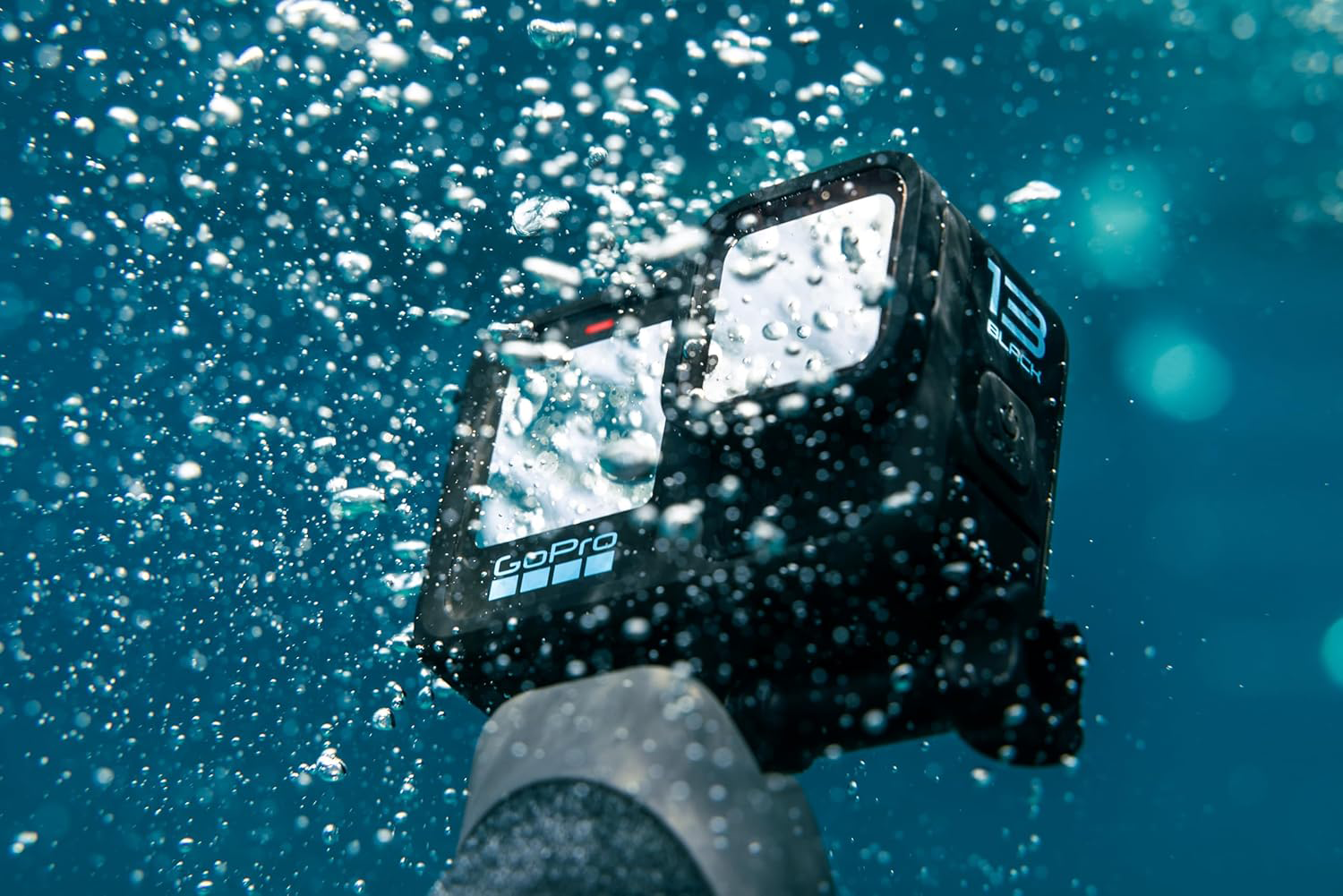 GoPro kamera víz alatt, felszálló buborékokkal és kék háttérrel.
