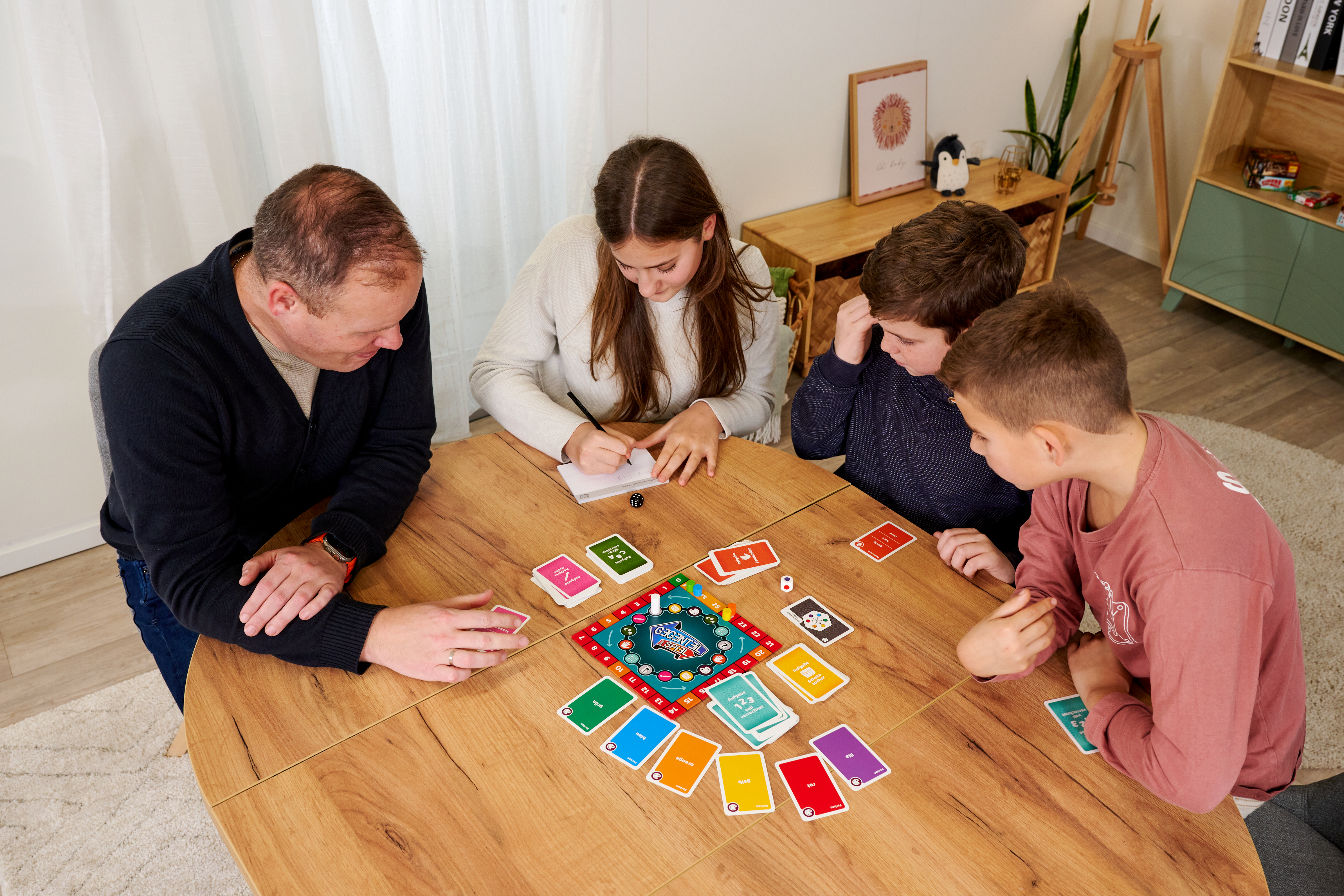 Vier Personen spielen ein Brettspiel an einem Holztisch. Viele Karten liegen auf dem Tisch.