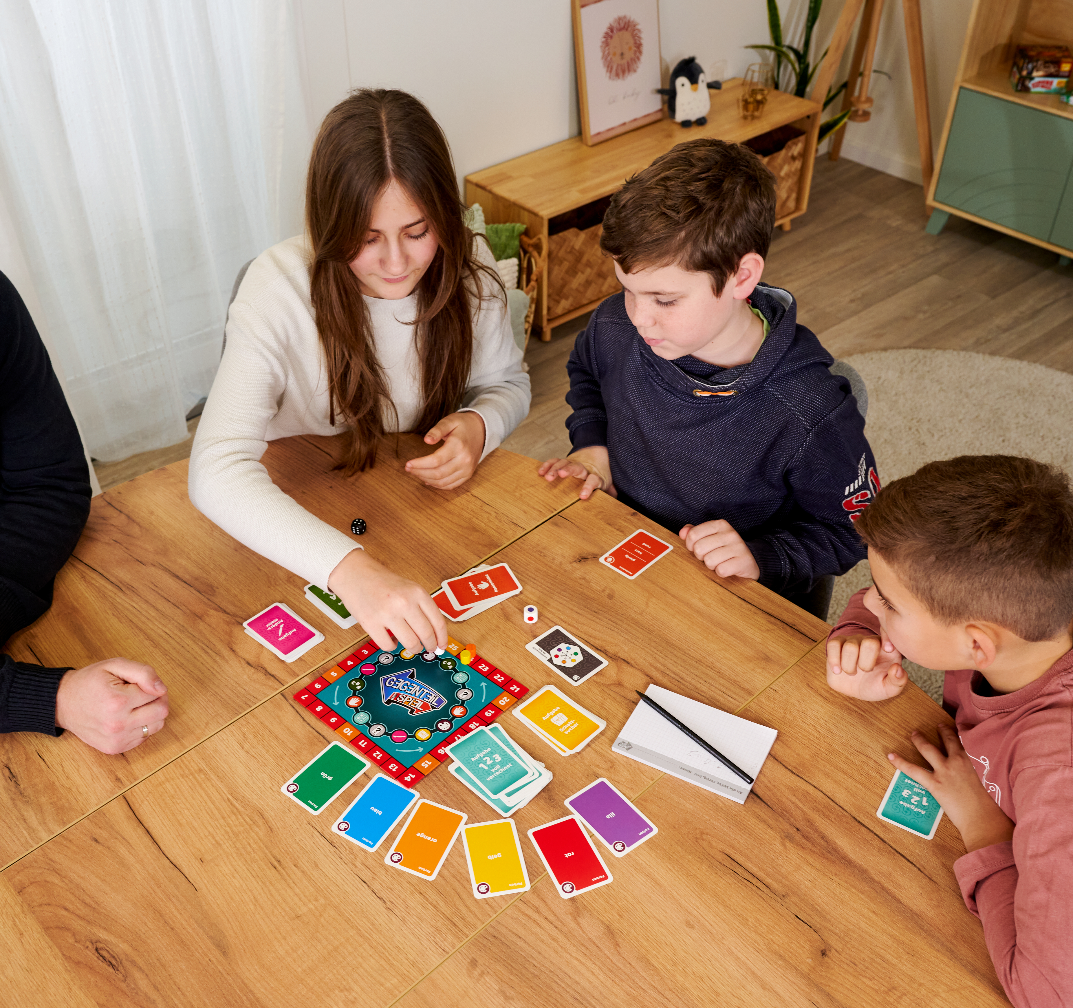 Kinder spielen ein Brettspiel mit bunten Karten auf einem Holztisch.
