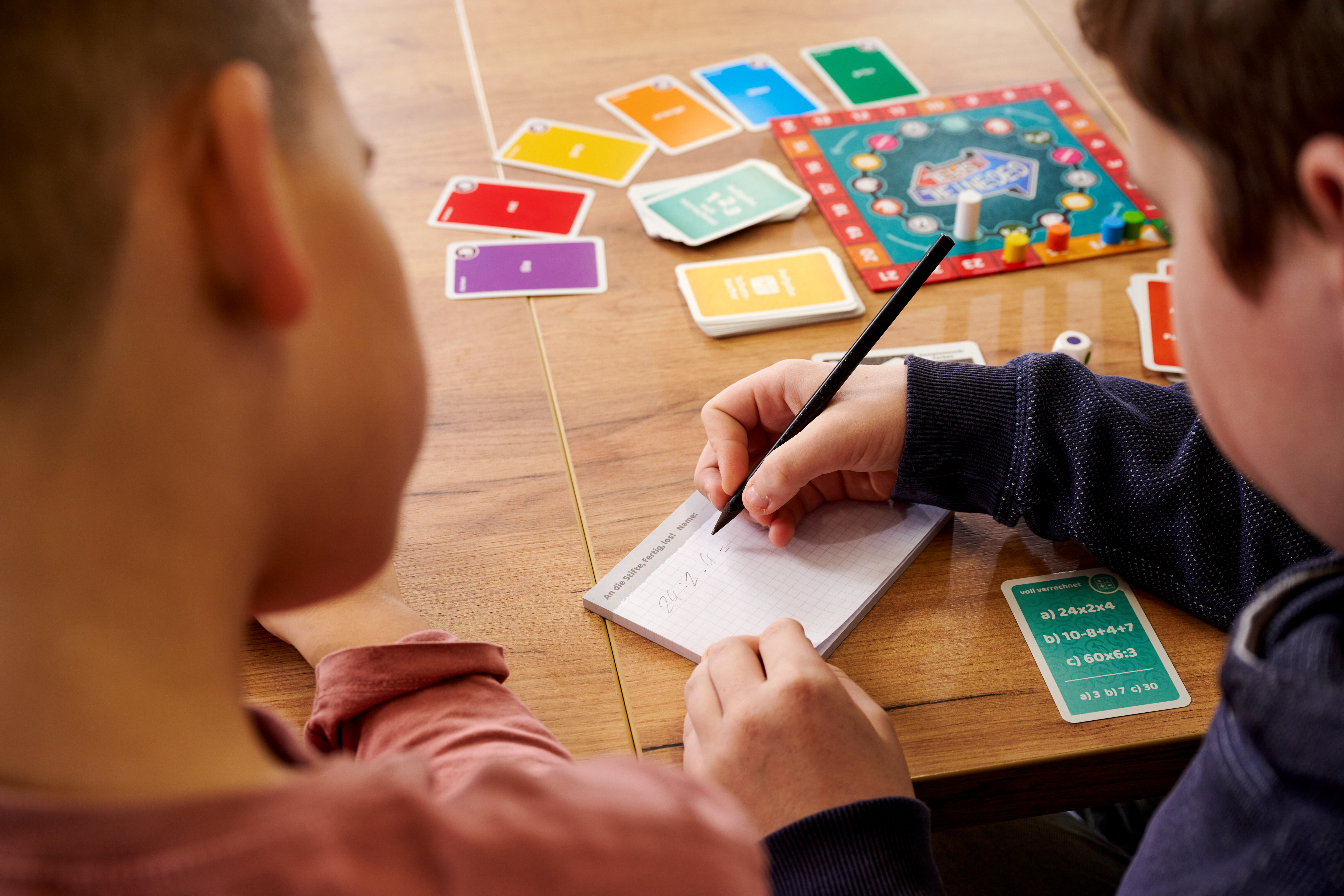 Kinder spielen ein Brettspiel und schreiben Aufgaben auf einem Notizblock.