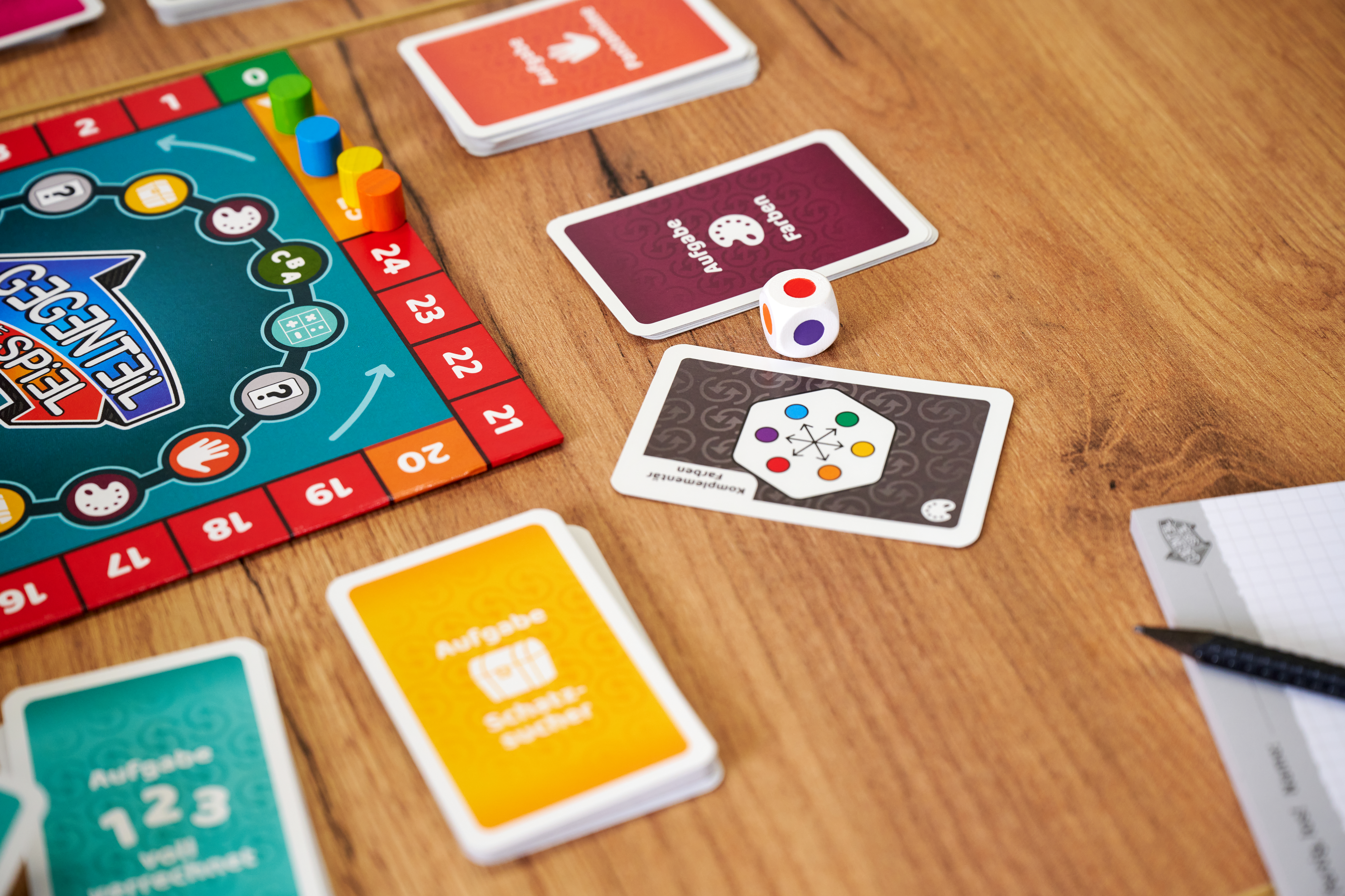Spielbrett mit Karten, Würfel und Spielfiguren auf Holztisch.