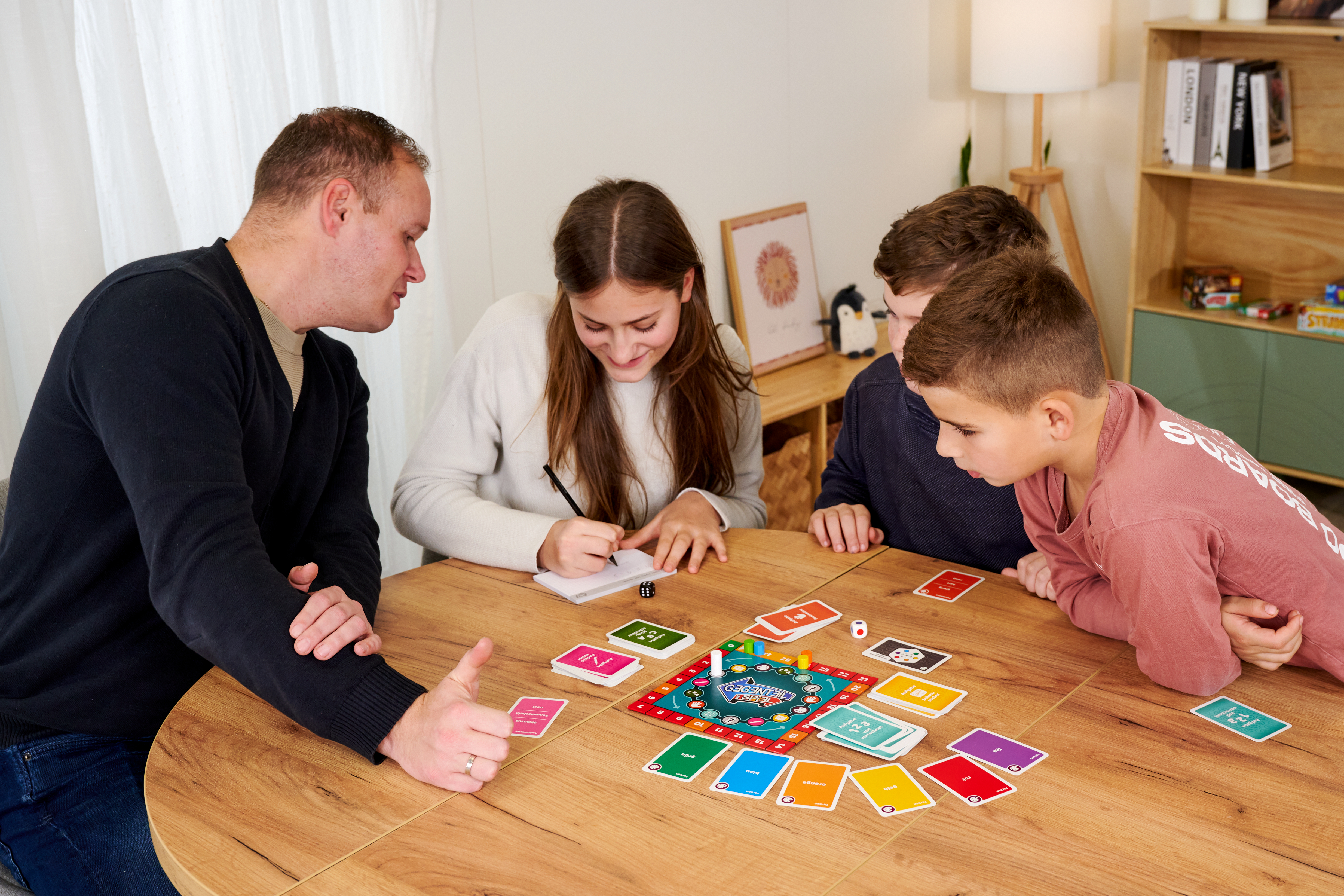 Familie spielt Brettspiel am Holztisch, Kinder schreiben und schauen.