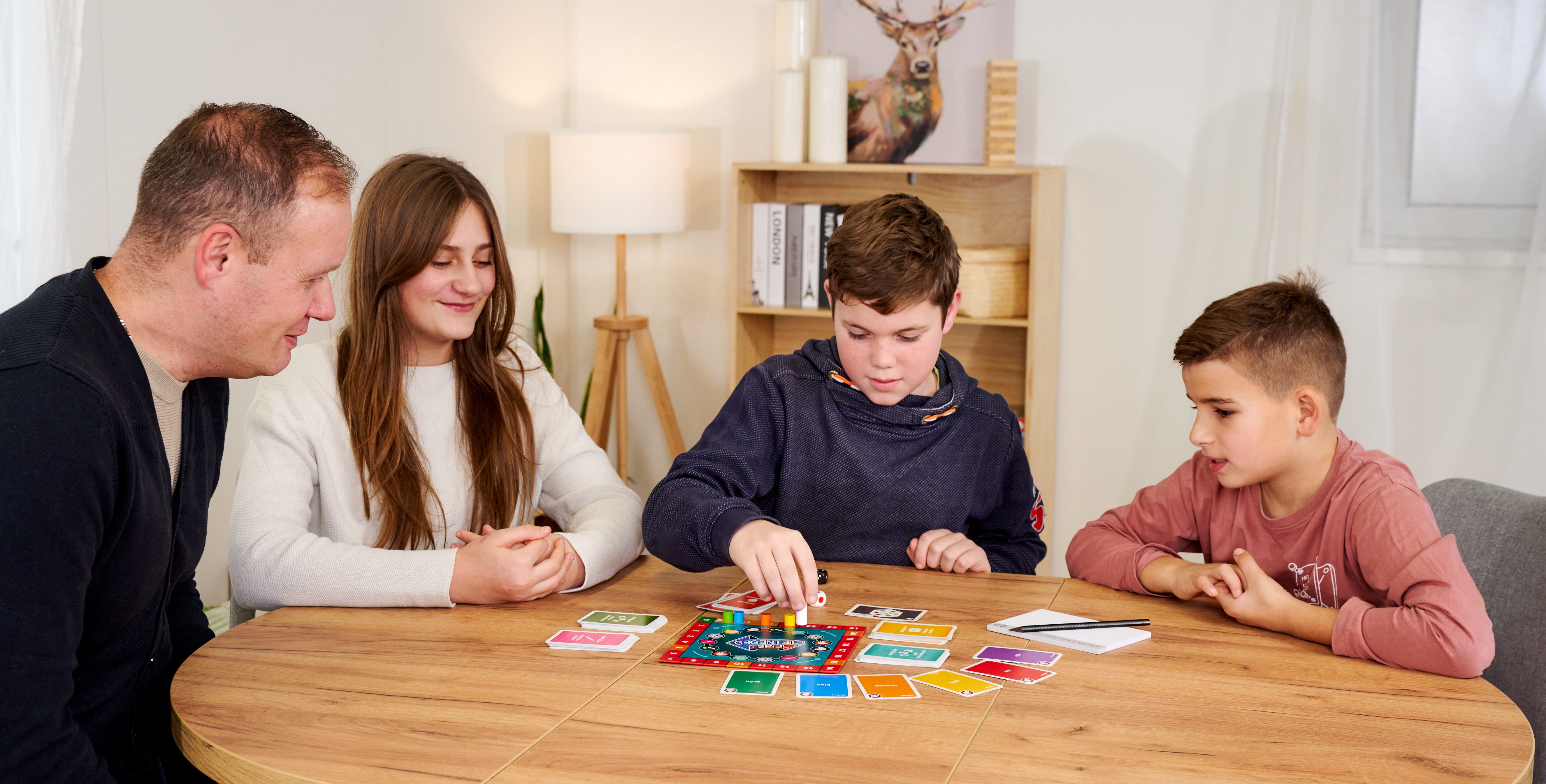 Familie spielt Brettspiel am Holztisch, Kinder und Erwachsener.