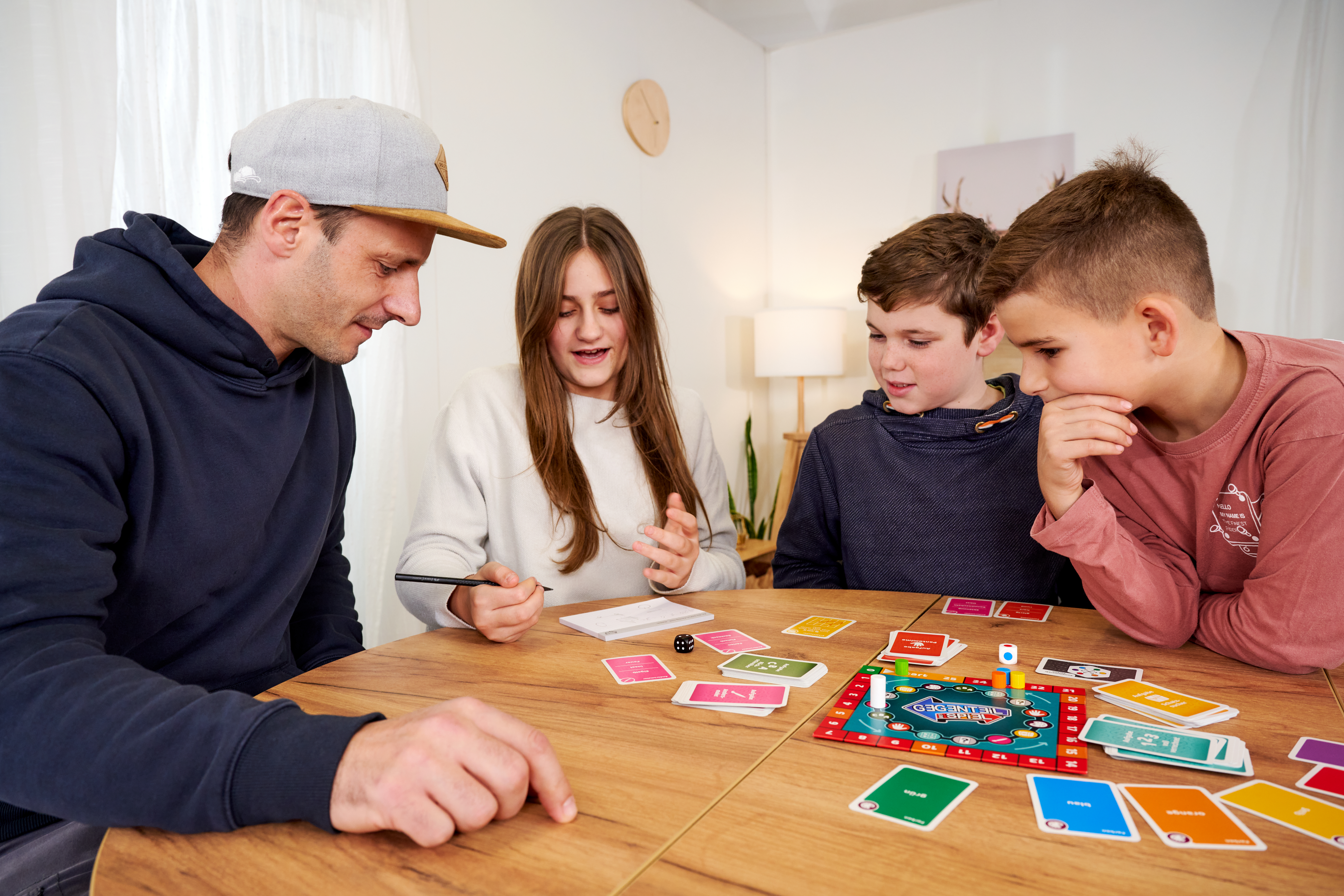 Vier Personen spielen ein Brettspiel mit Karten und Würfeln an einem Holztisch.