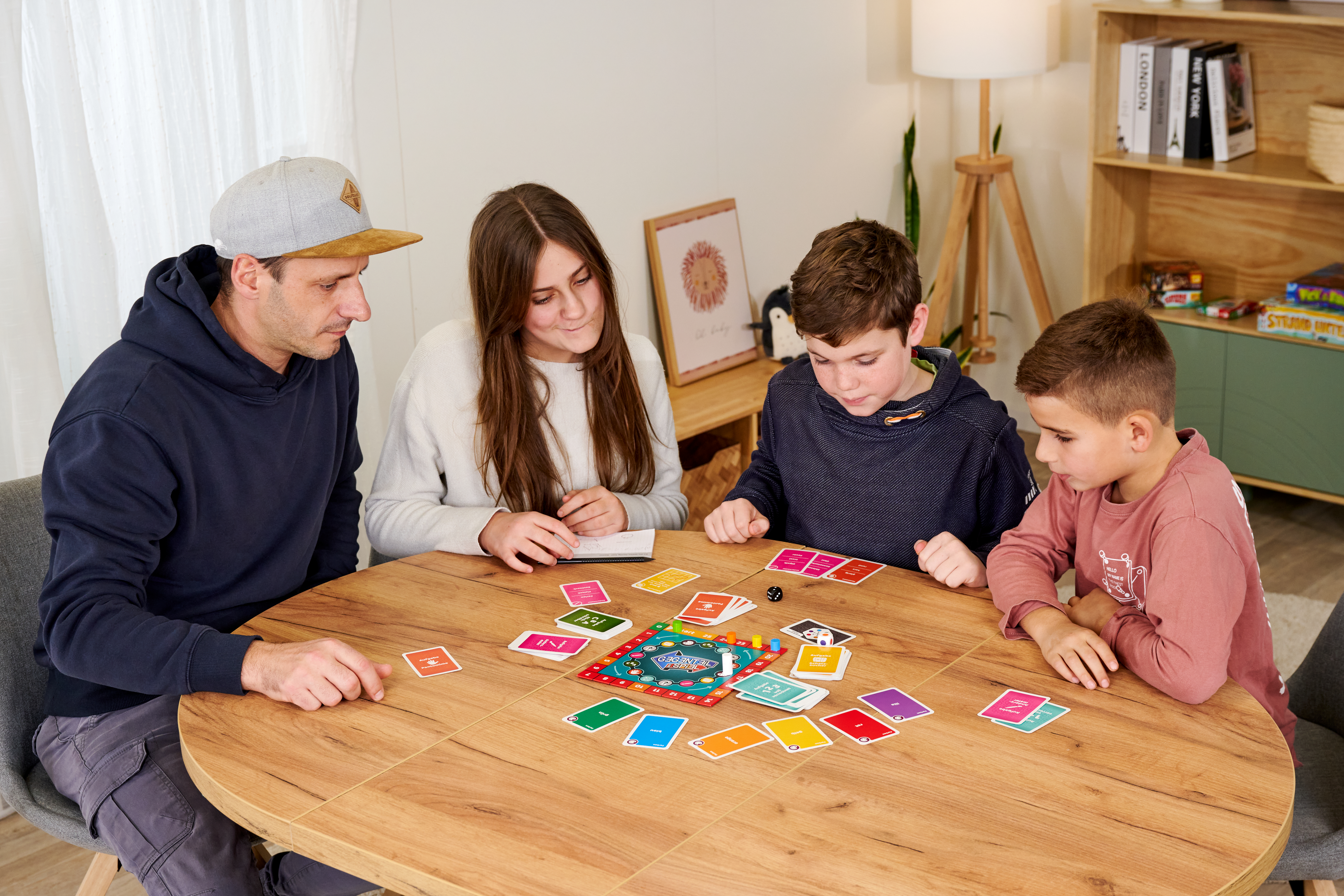 Familie spielt Brettspiel an Holztisch. Karten und Spielbrett sind ausgebreitet.
