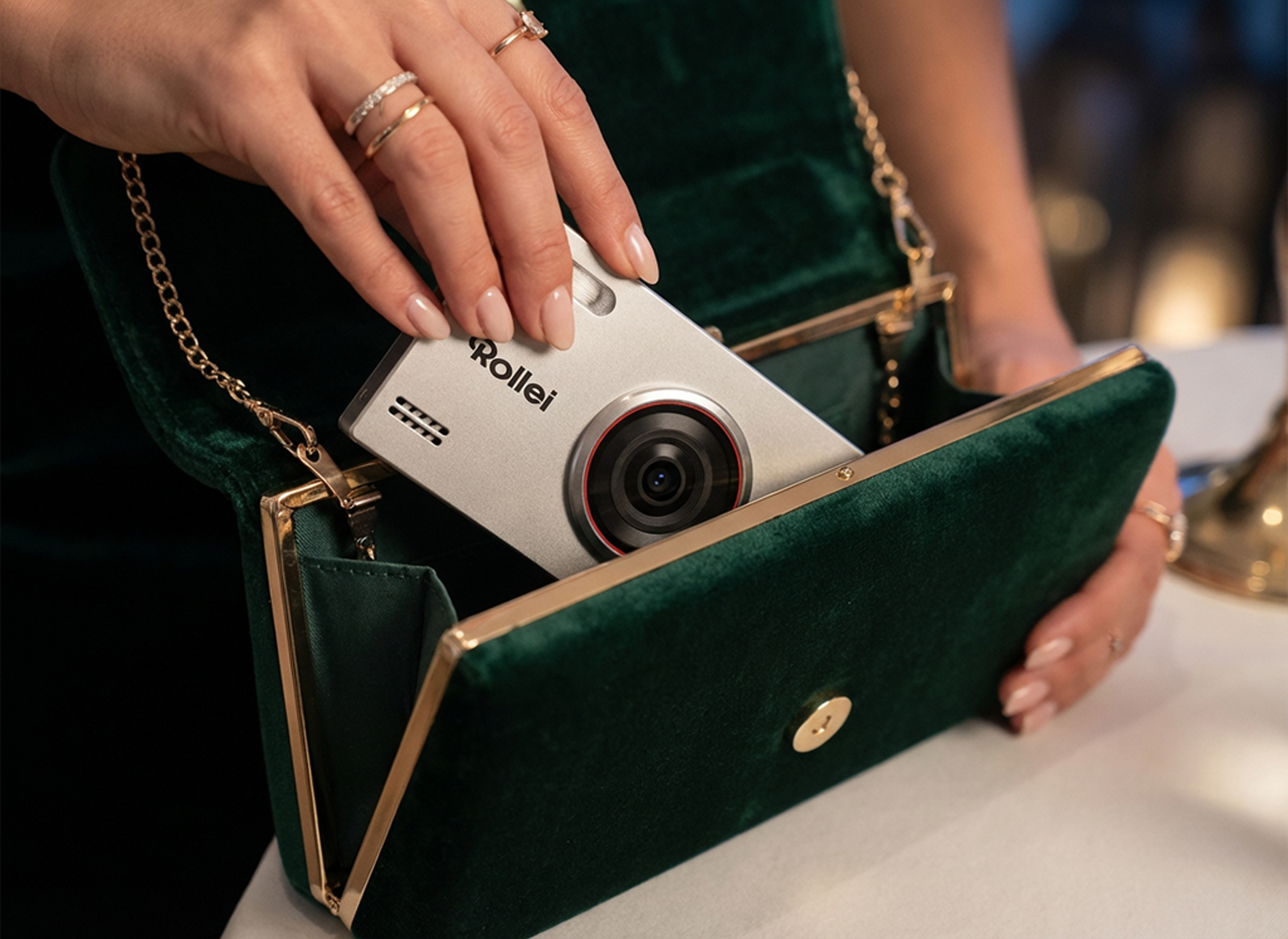 Eine Hand legt eine silberne Rollei Kamera in eine grüne Samtclutch.