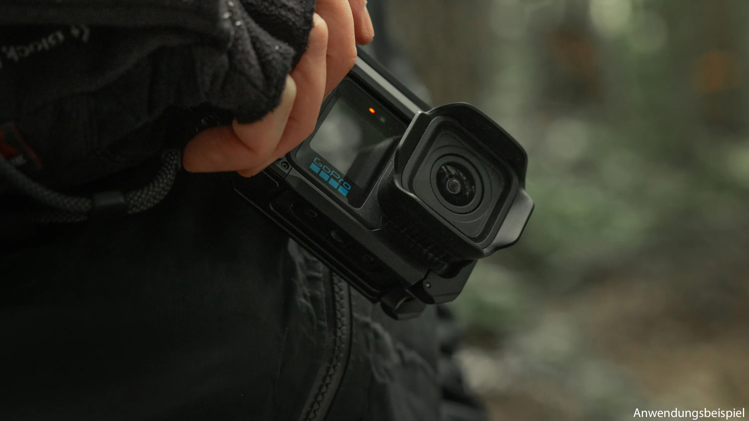 Egy kéz egy piros fényű fekete GoPro kamerát tart. A háttér elmosódott.
