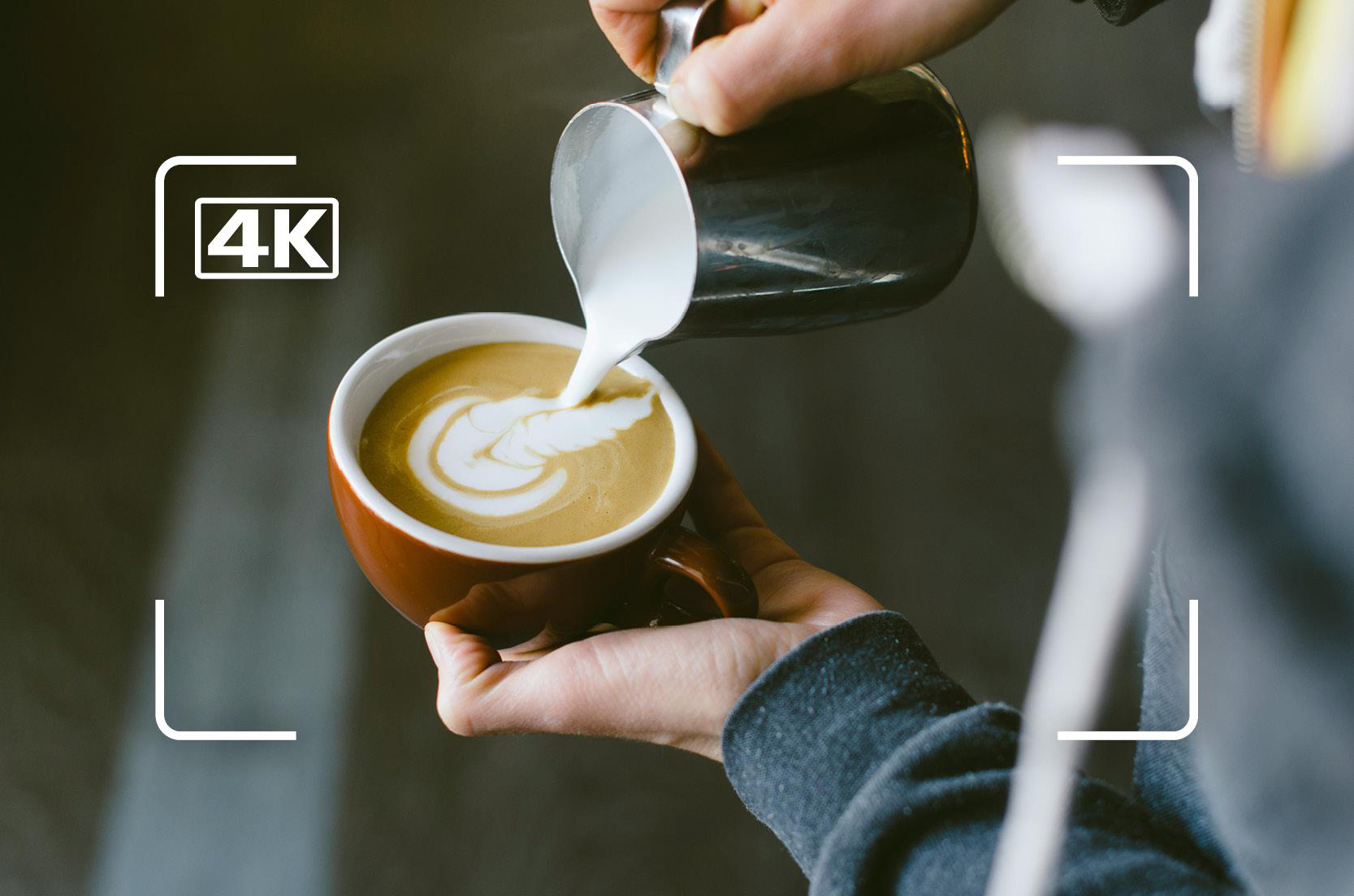 Ein Barista gießt Milch in eine braune Tasse Kaffee mit Latte Art.