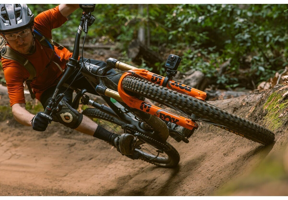 Egy narancssárga felsős mountain bike-os egy kanyarban dől egy földúton. Akciókamera a kormányra szerelve.