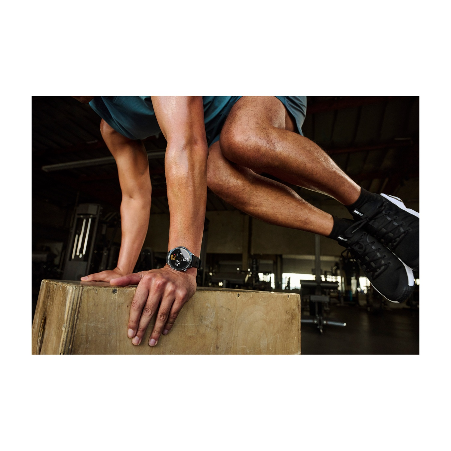 Uomo che fa salti sul box in palestra. Primo piano su gambe e braccia, indossa uno smartwatch.