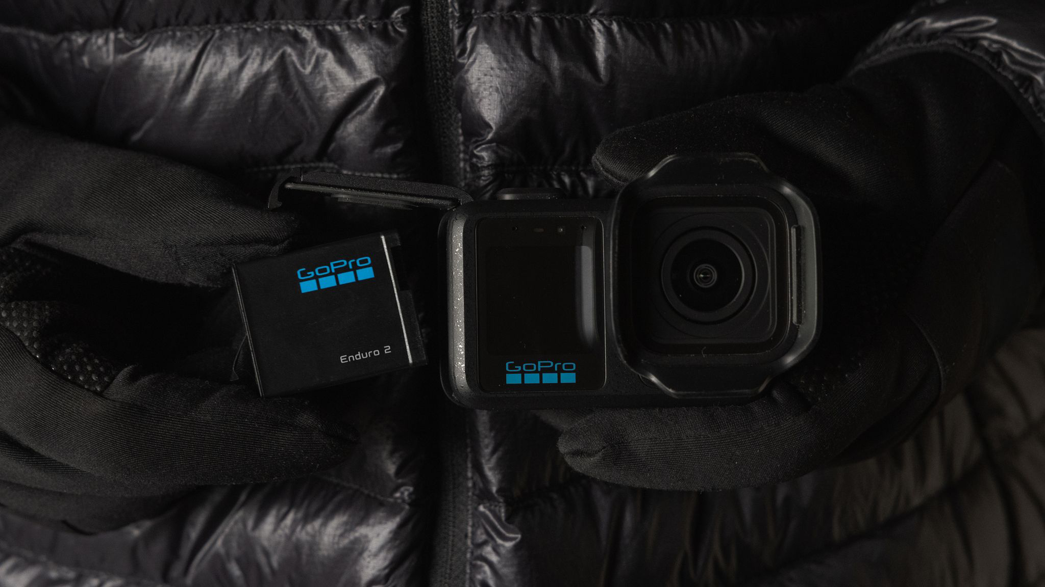 Fekete kesztyűs kezek GoPro kamerát és akkumulátort tartanak.