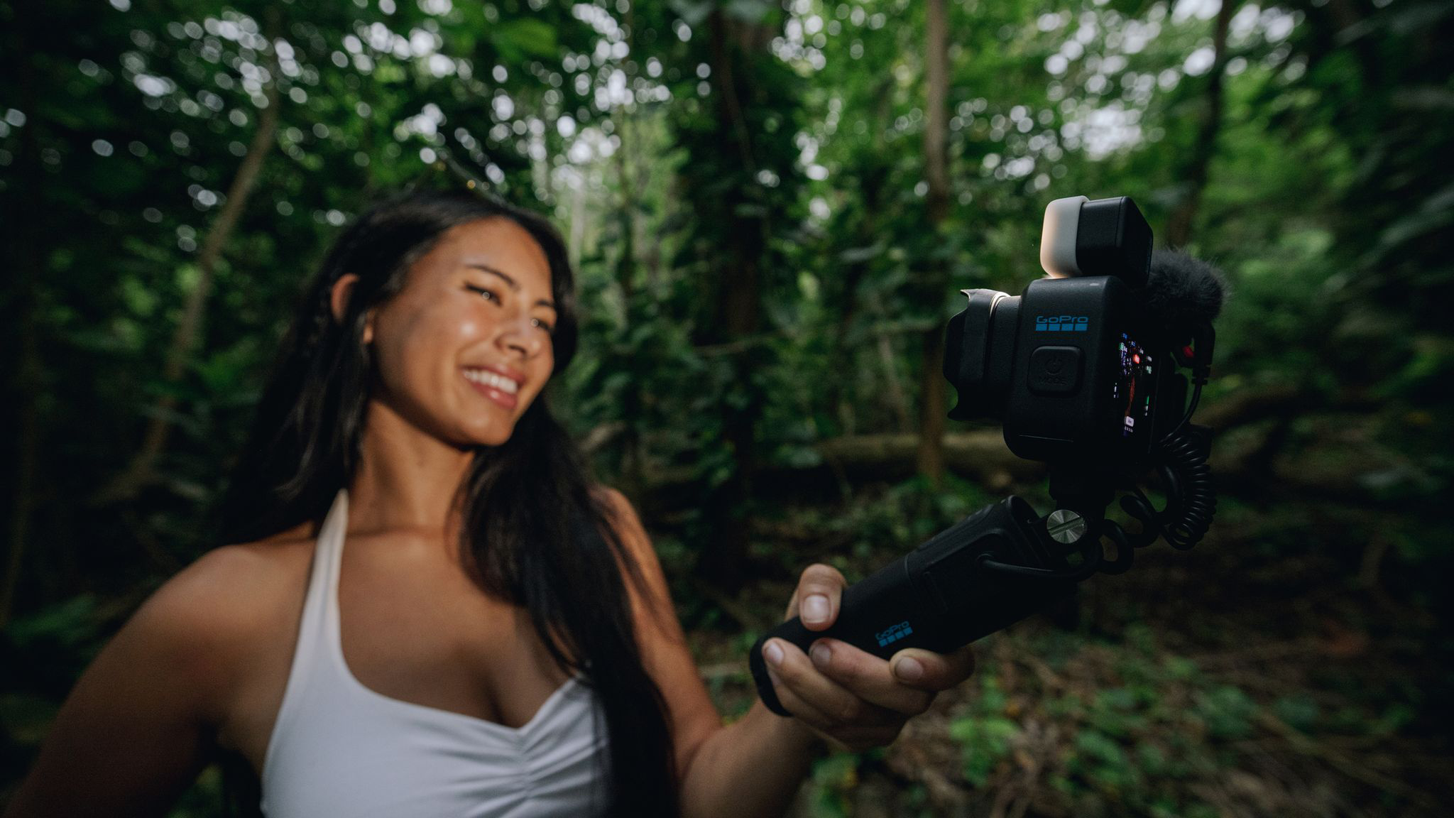 Egy nő GoPro-val filmez az erdőben. Mosolyog.