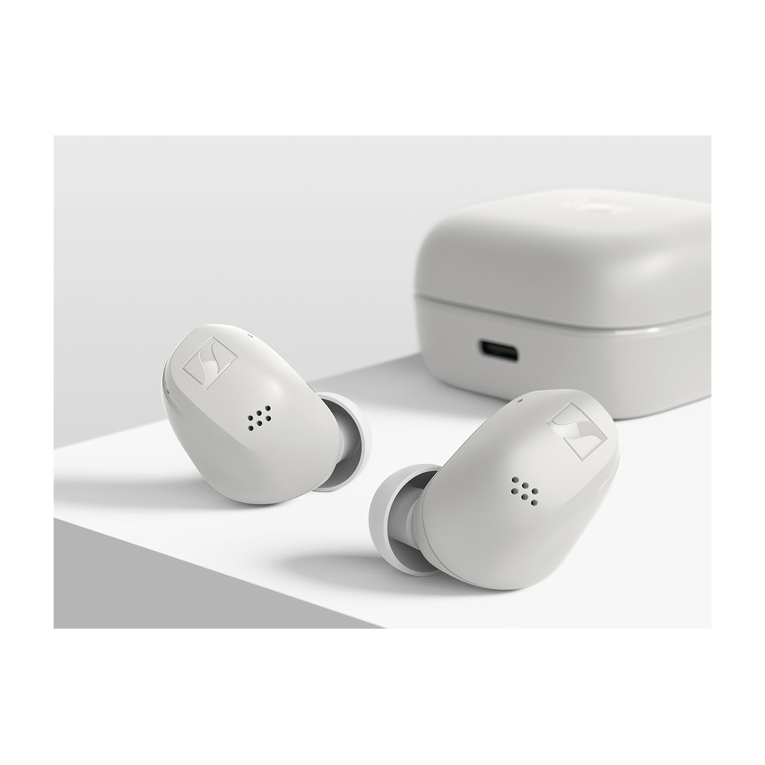 Due auricolari Sennheiser bianchi e una custodia di ricarica su sfondo bianco.