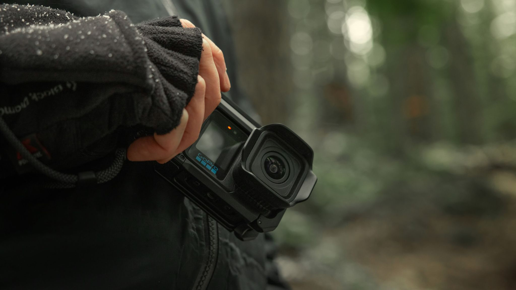 Egy fekete kesztyűs kéz fekete GoPro kamerát tart az erdőben.