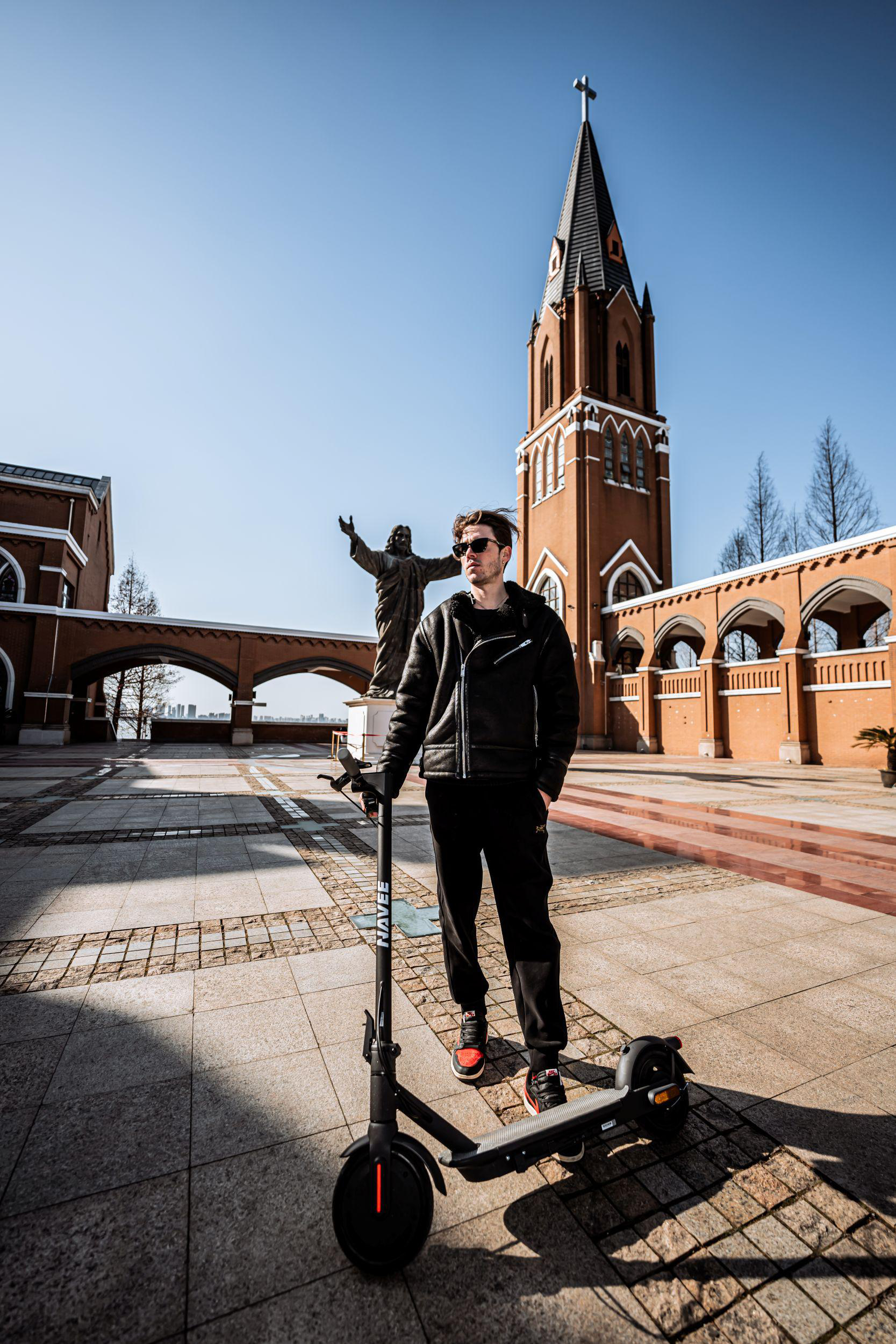 Ein Mann mit einem Roller steht vor einer Kirche mit einer Statue von Jesus.
