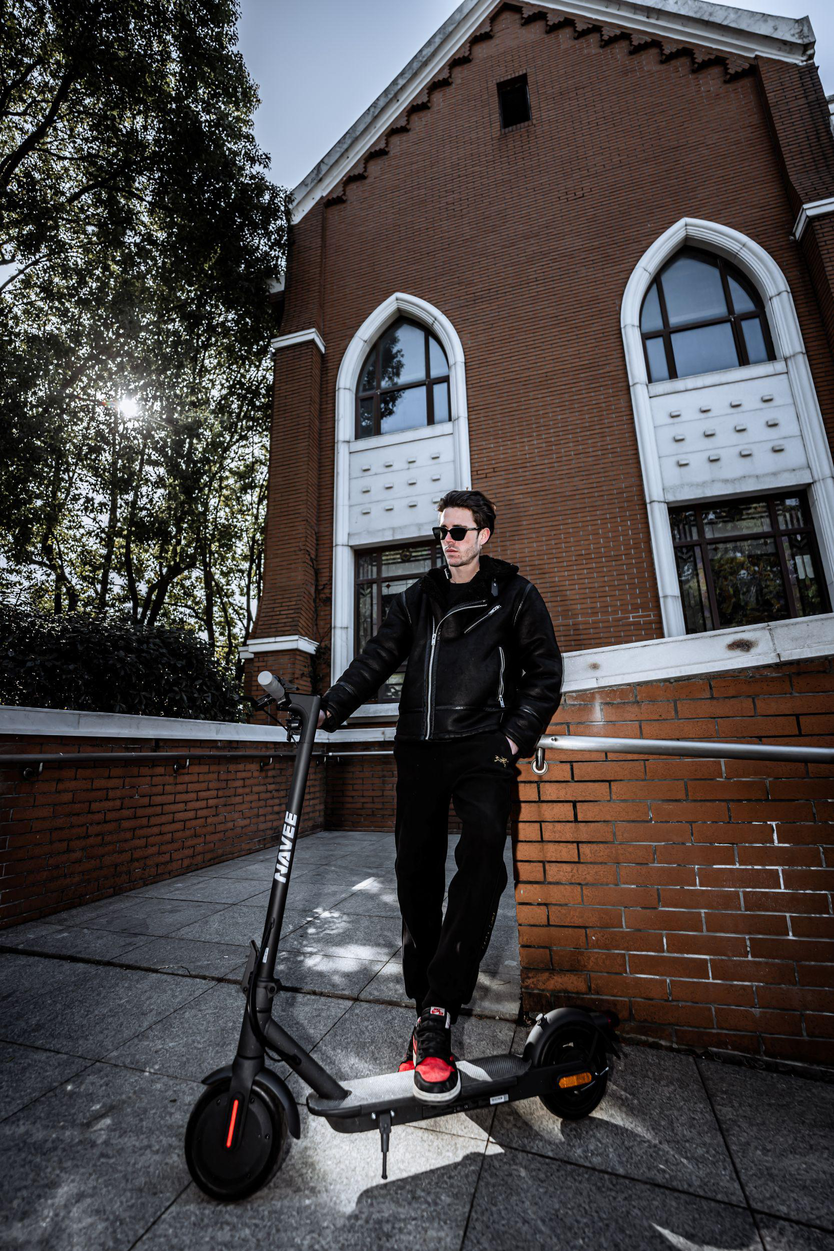 Mann mit E-Scooter vor Backsteingebäude mit Bäumen.