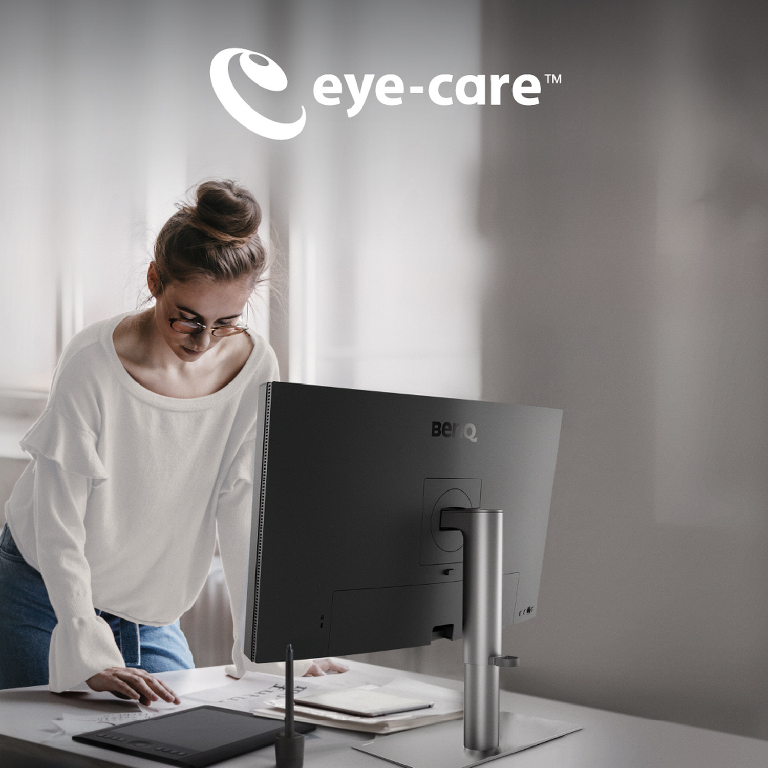 Una donna si china su una scrivania con un monitor e un tablet.