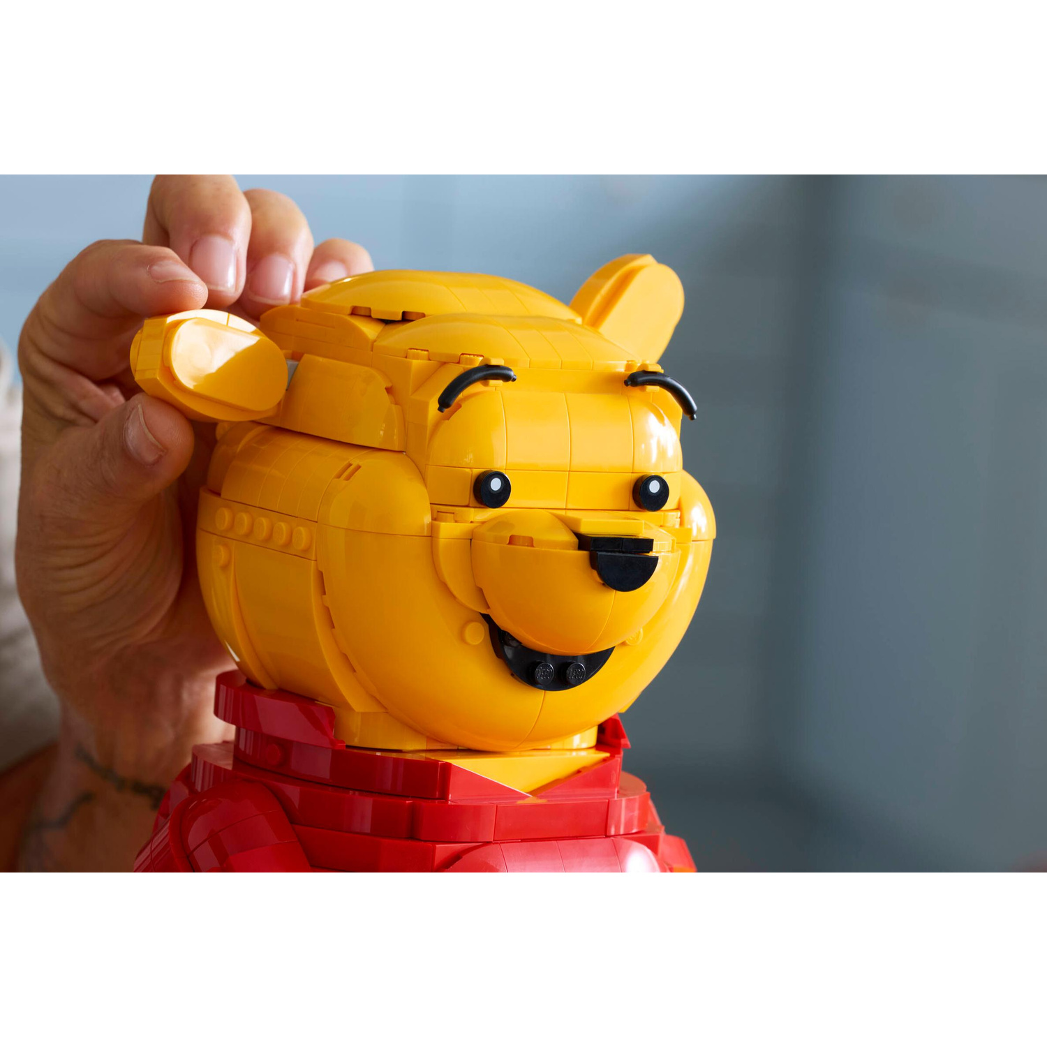 Una persona sta costruendo un Winnie the Pooh Lego giallo con una camicia rossa.