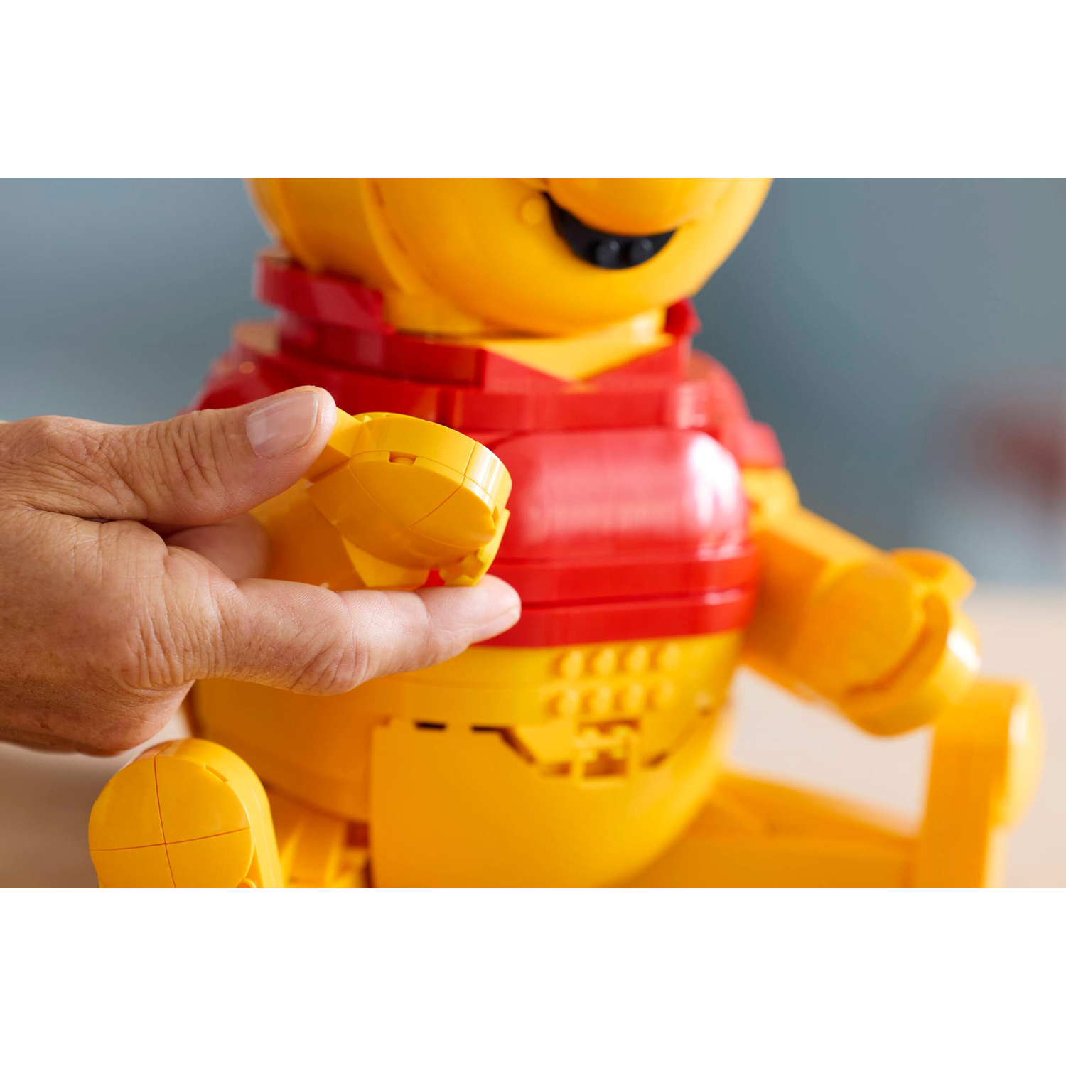 Una mano che tiene un pezzo Lego giallo davanti a un personaggio Lego di Winnie the Pooh.
