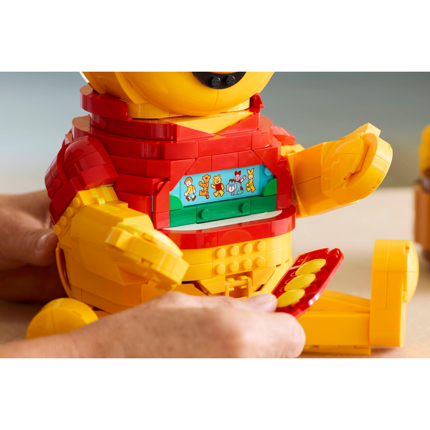 Un Winnie the Pooh Lego rosso e giallo assemblato da mani. Uno scomparto mostra figure.