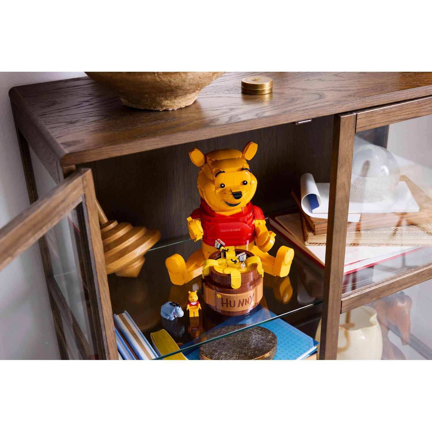 Un Winnie the Pooh Lego siede su un vaso "Hunny" in un mobiletto di legno.