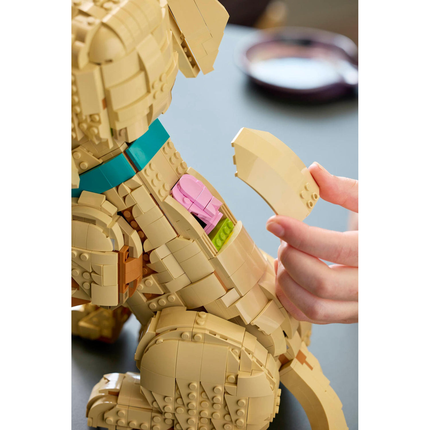 Un cane Lego color camoscio viene assemblato, con un osso Lego rosa all'interno.