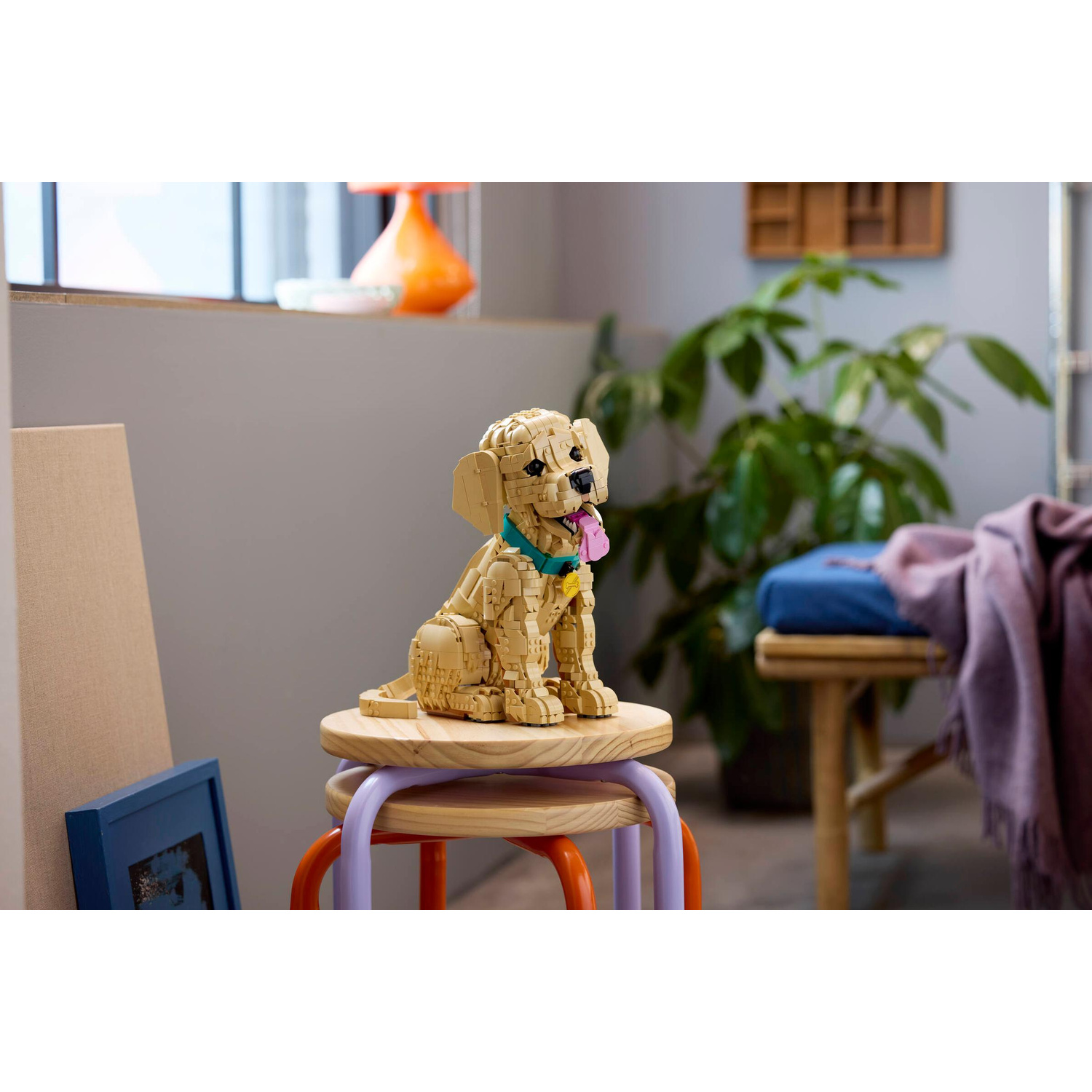 Un cane Lego è seduto su uno sgabello. Piante e mobili sullo sfondo.