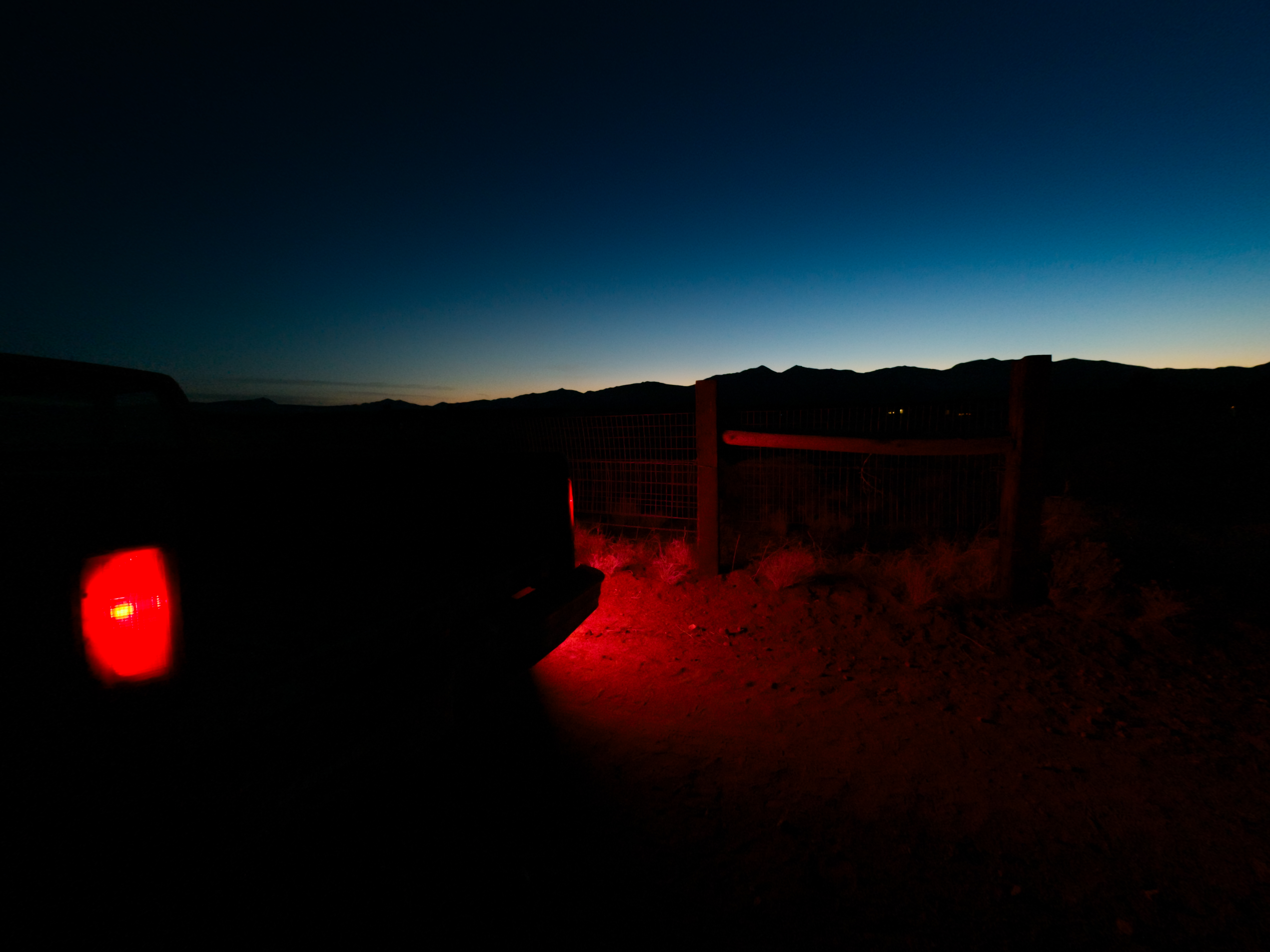 Rotes Rücklicht eines Autos leuchtet auf einem Feldweg bei Dämmerung.