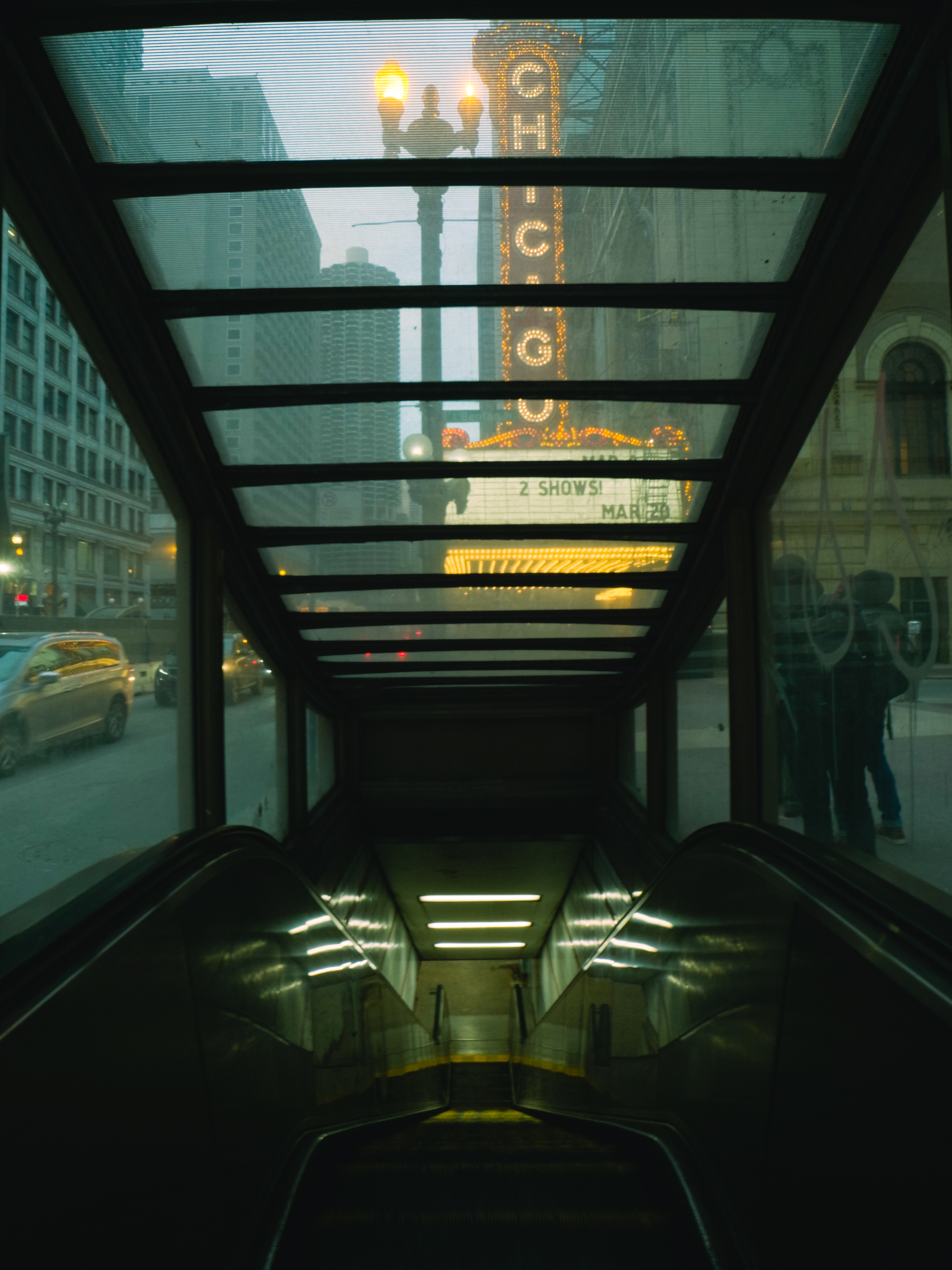 Ein Eingang zu einer U-Bahn-Station mit Rolltreppe, Blick auf beleuchtete Gebäude und die Aufschrift "CHICAGO".