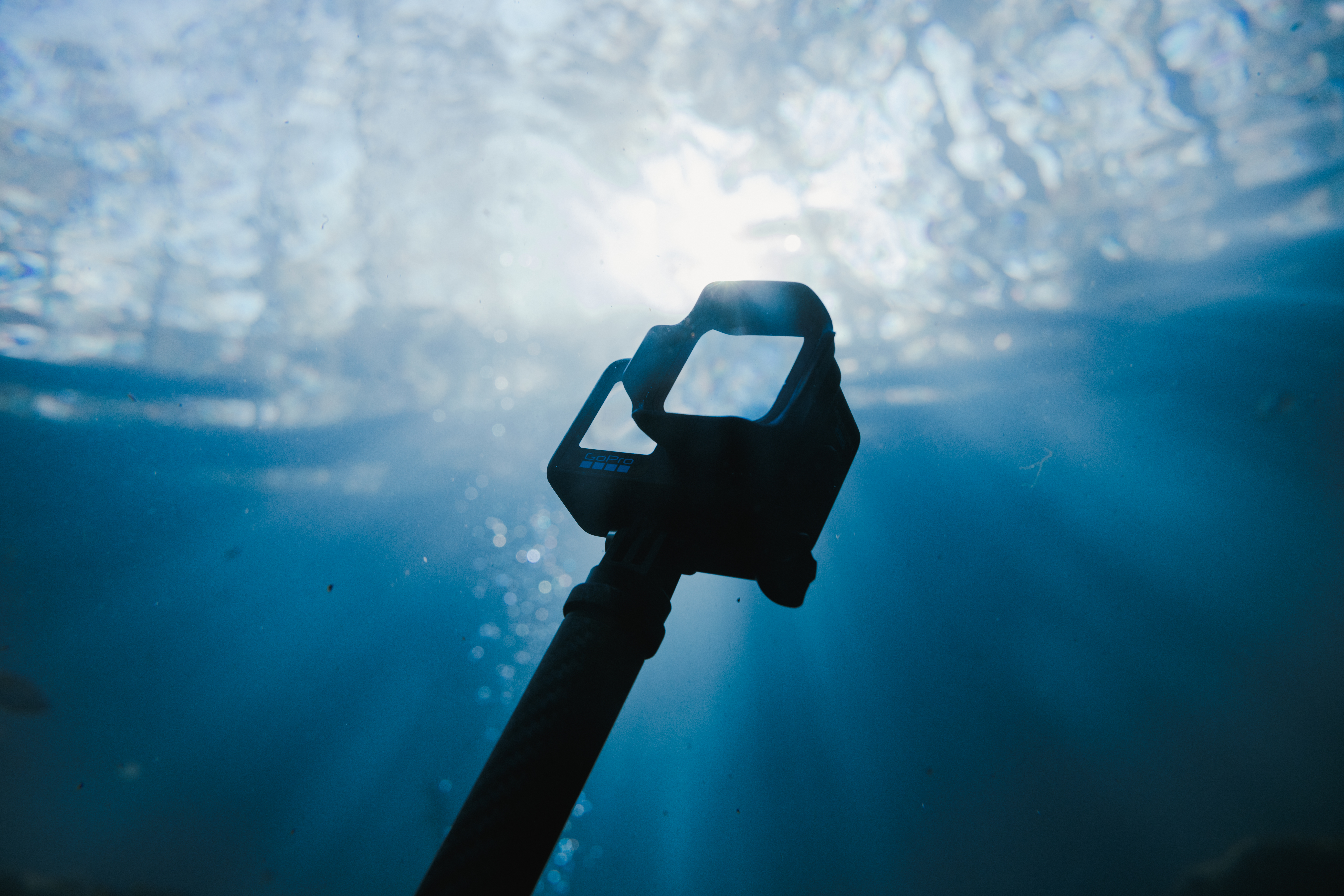 Unterwasseraufnahme einer GoPro-Kamera an einem Griff, Sonnenlicht bricht durch das Wasser.