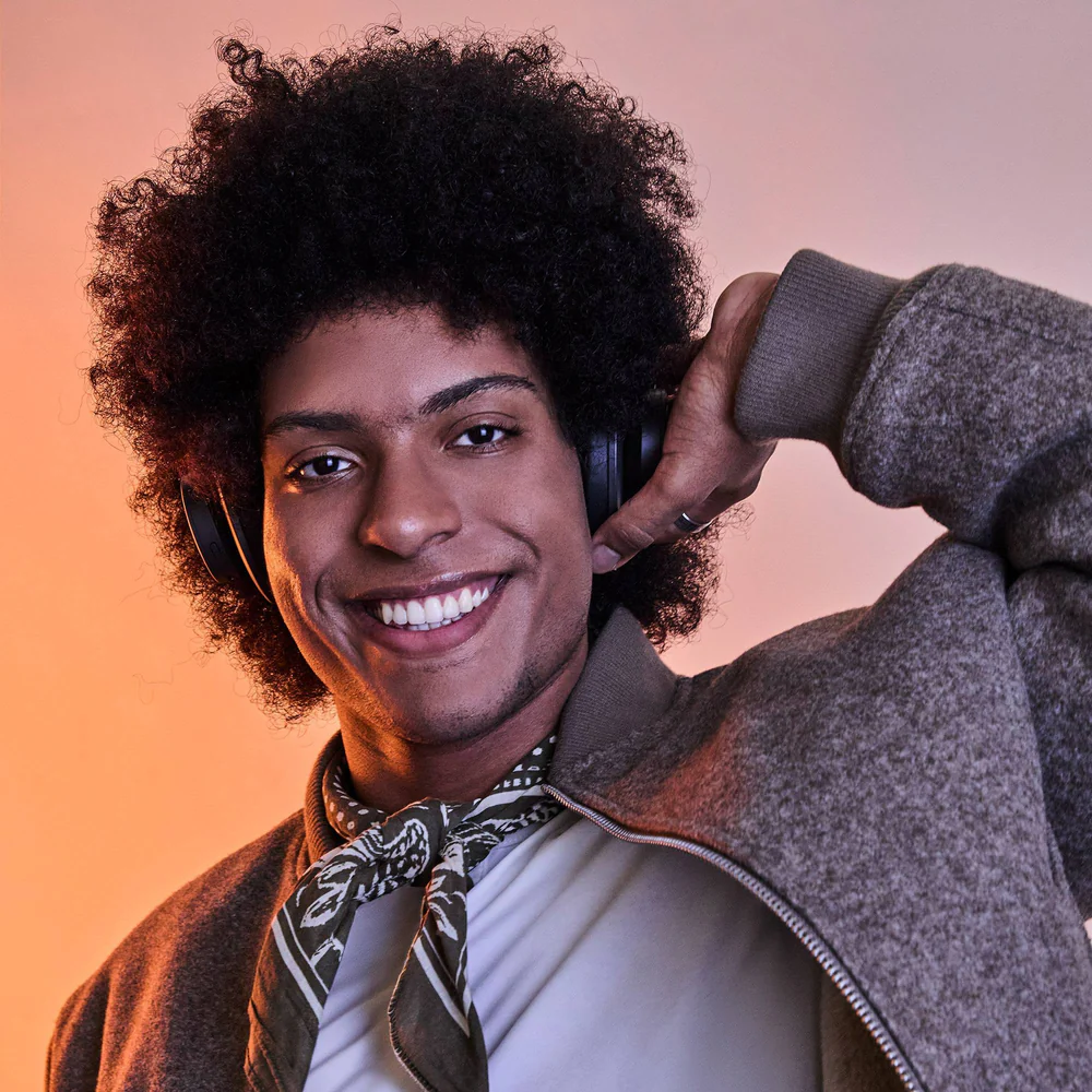 Afro frizurás férfi mosolyog, fejhallgatót és bomber dzsekit visel.