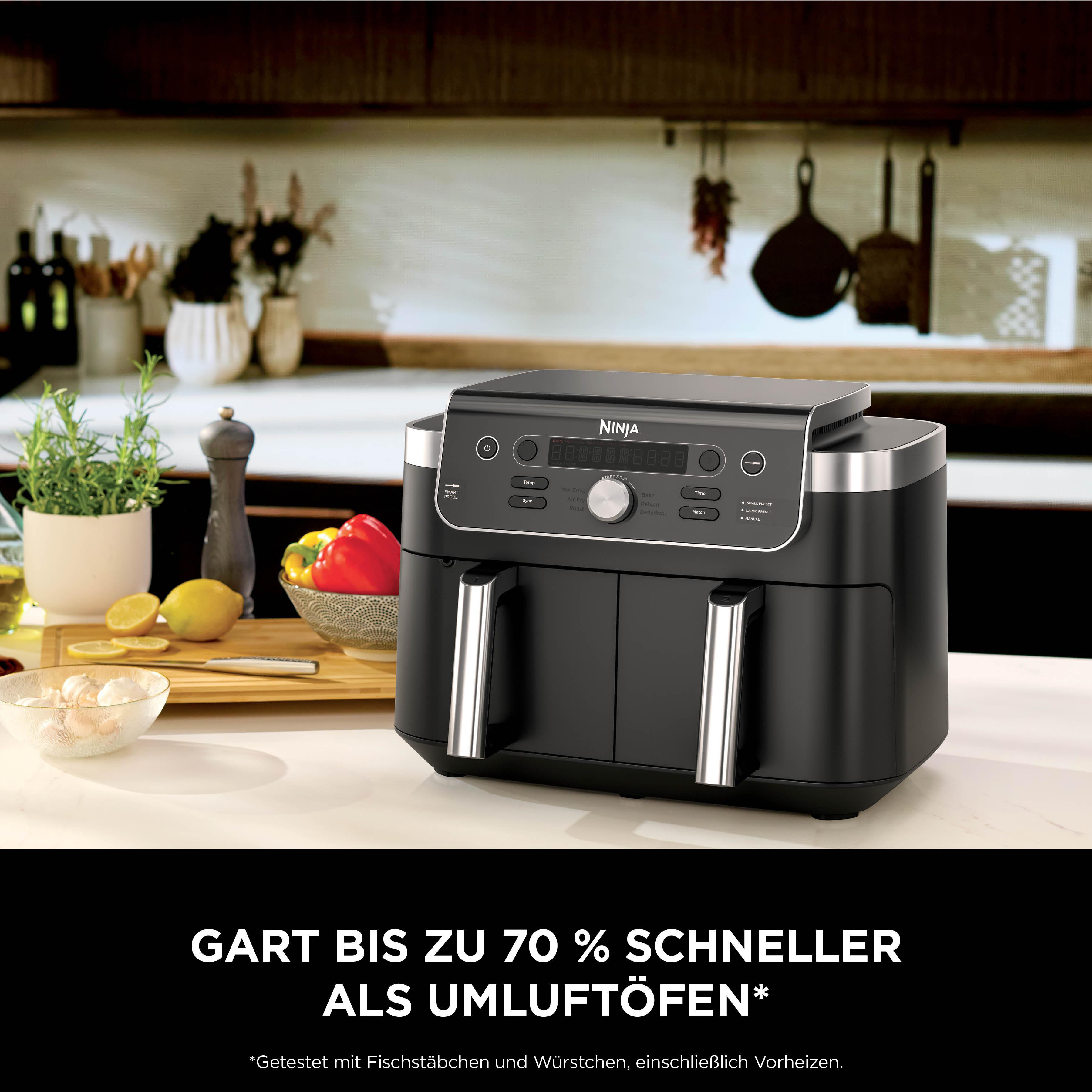 Schwarzer Ninja Heißluftfritteuse mit Kochutensilien und Gemüse auf der Arbeitsplatte.