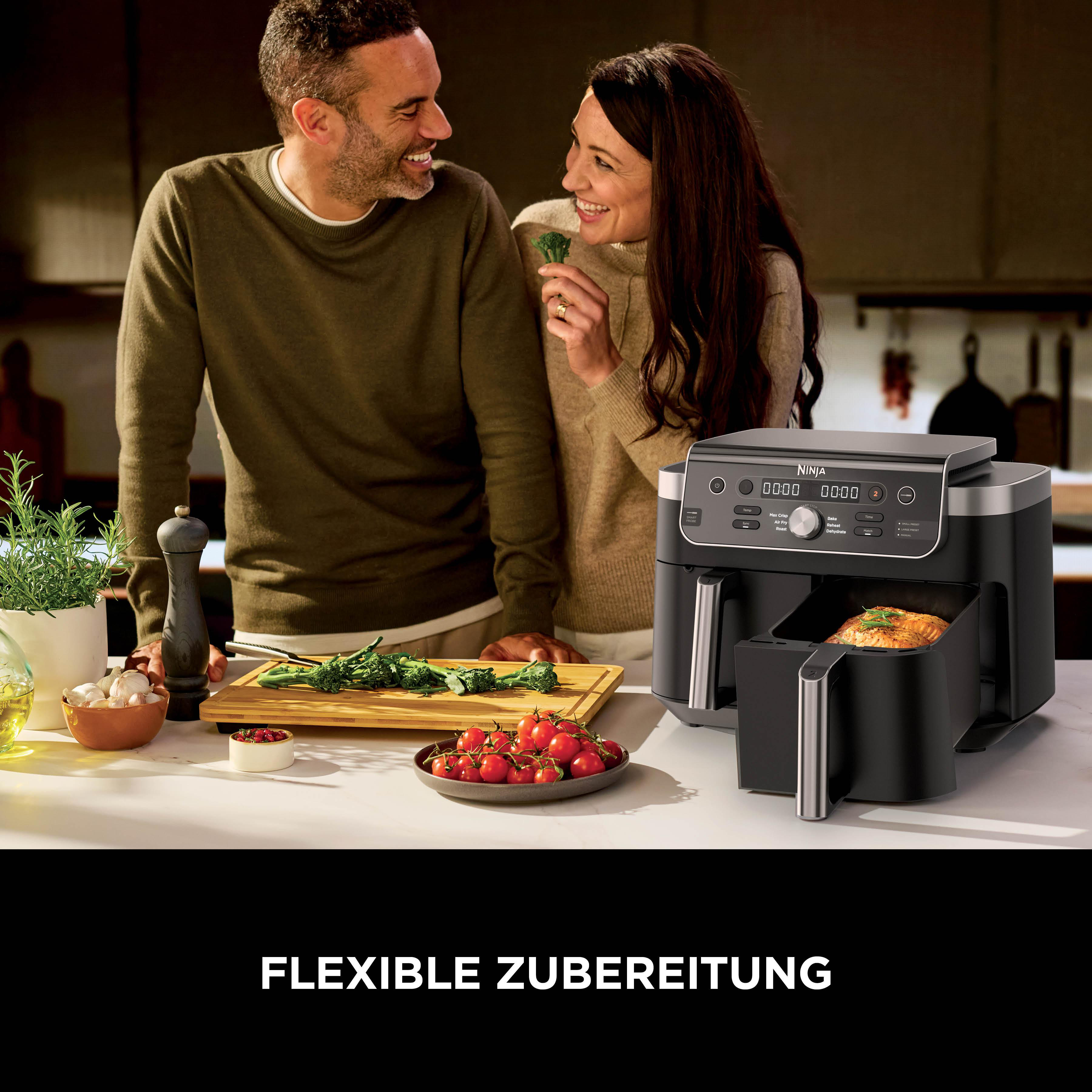 Ein Paar lacht, während ein Ninja Air Fryer daneben steht. Auf dem Tisch sind Tomaten und Brokkoli.