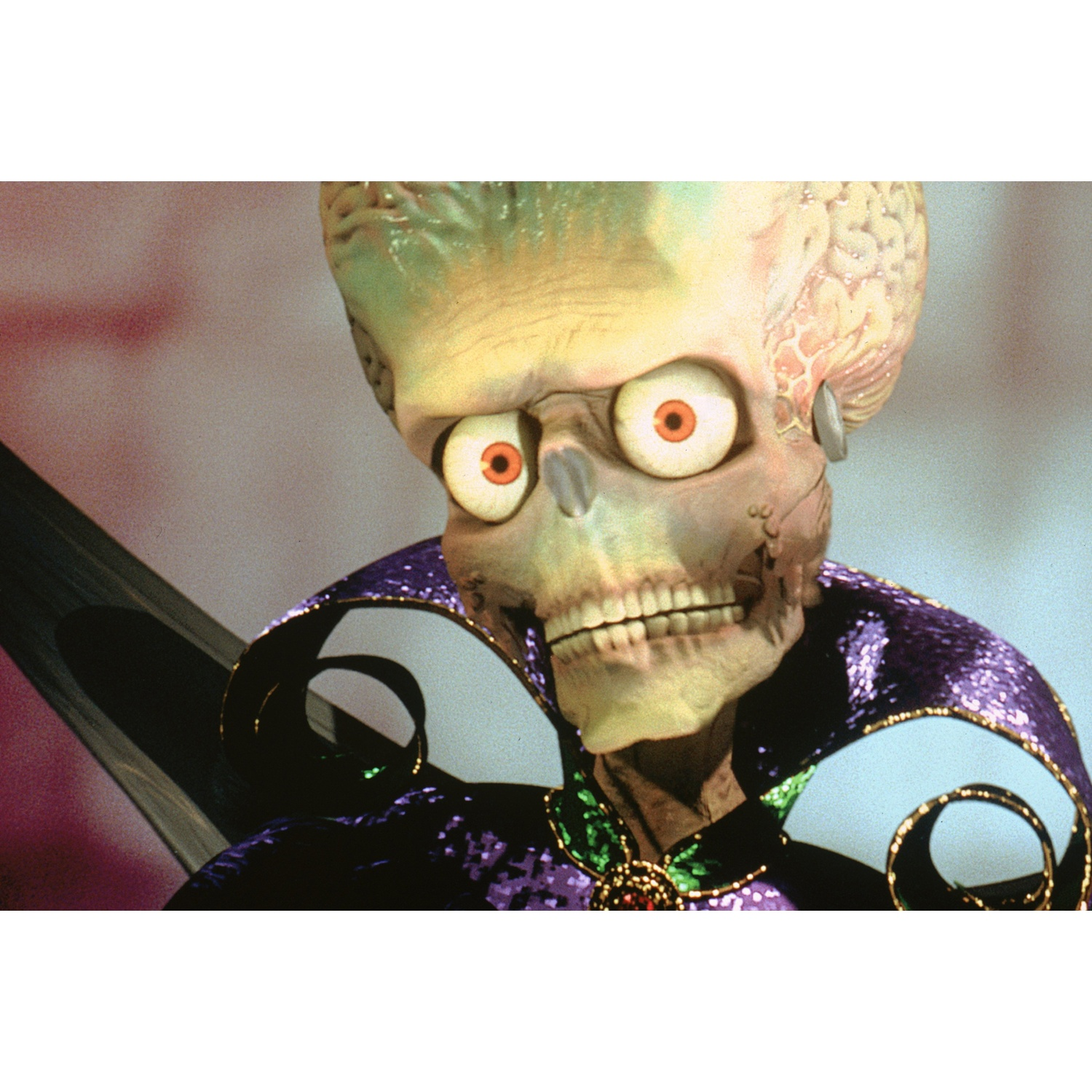 Een groene alien met grote ogen en een paarse cape.