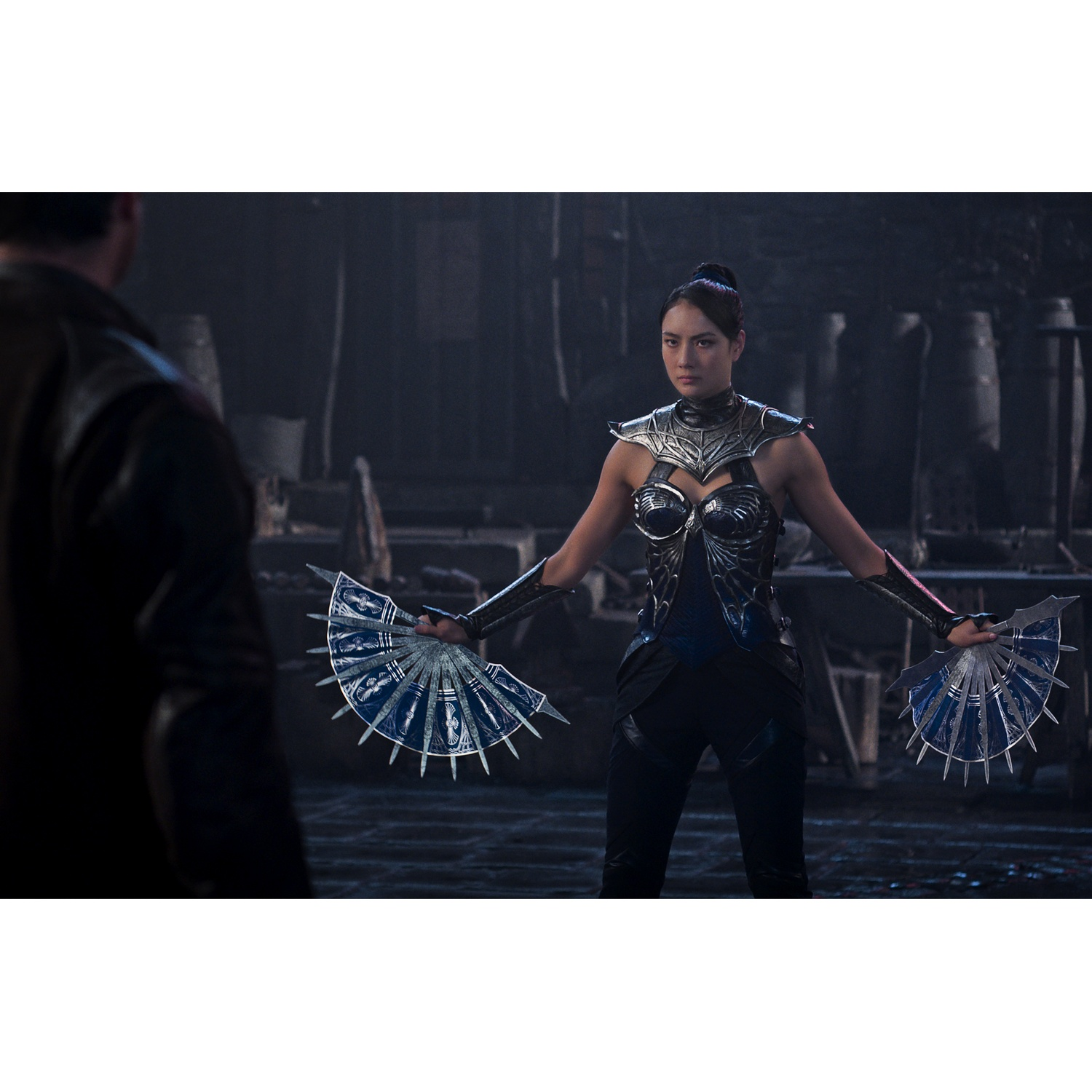 Femme en armure tient des éventails à lames; homme au premier plan.