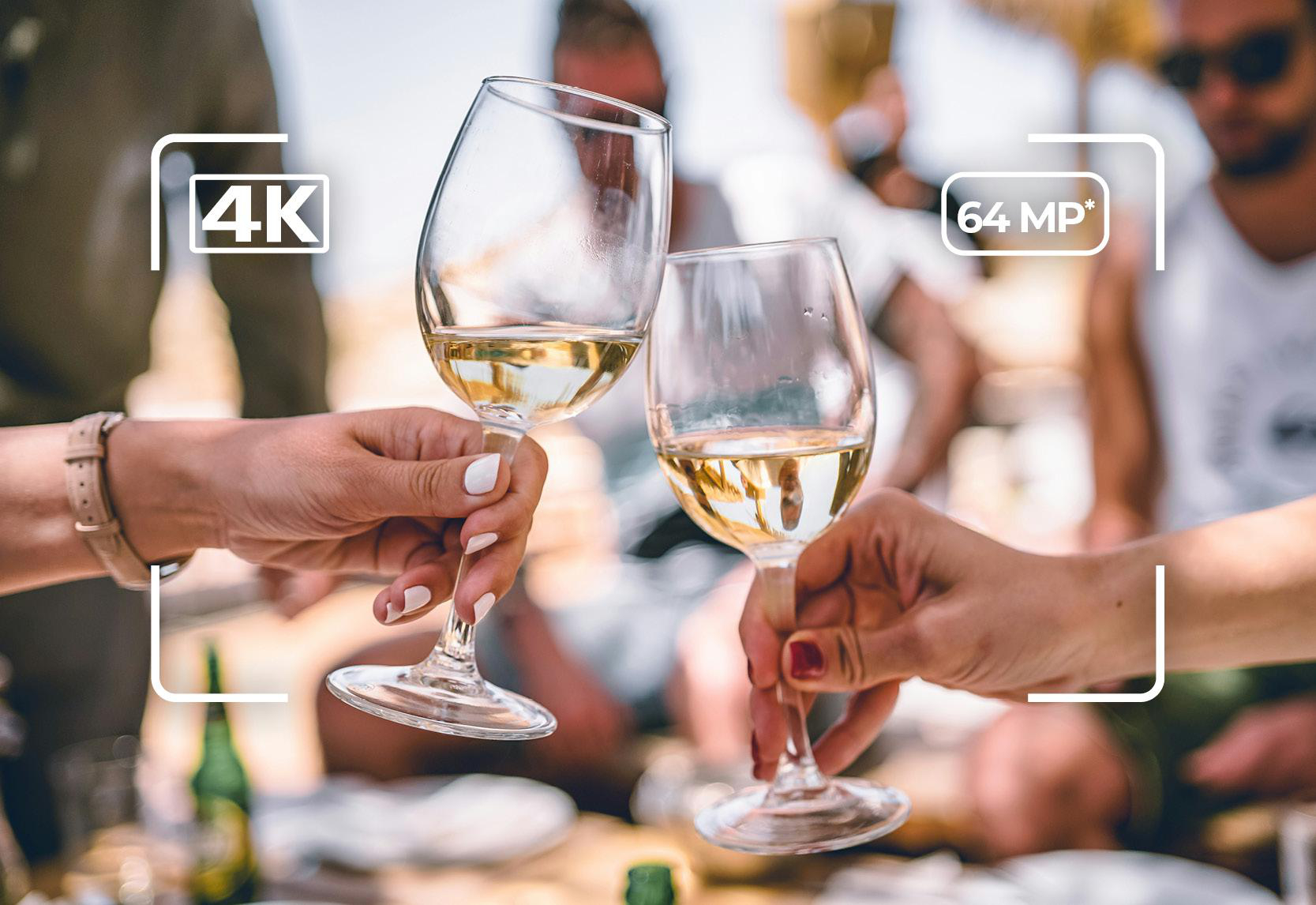 Zwei Gläser Weißwein werden von Händen gehalten, mit Personen im Hintergrund.