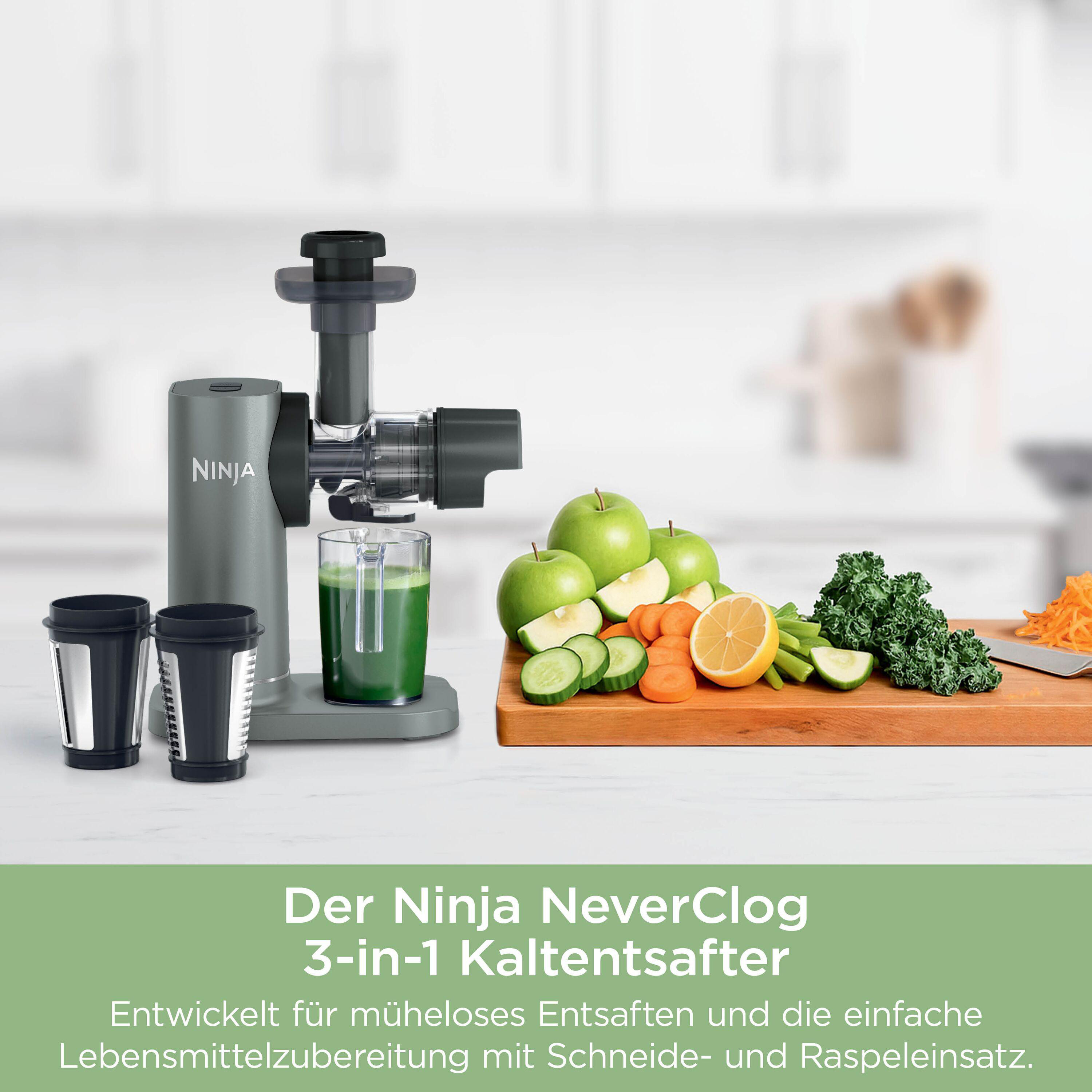 Ein Ninja Entsafter mit Glas, Äpfeln, Gurken, Karotten und Grünkohl auf einem Schneidebrett.