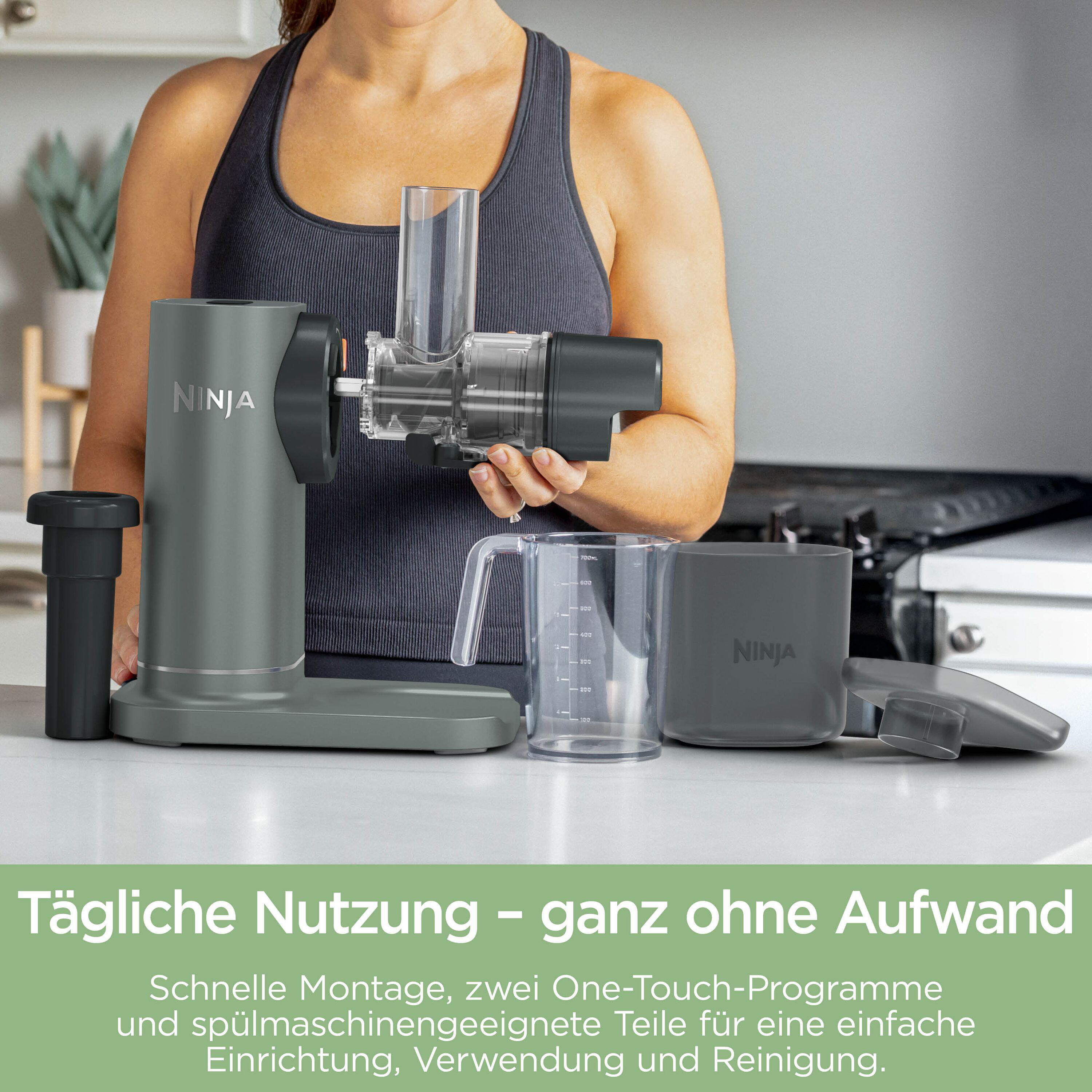 Eine Frau hält einen Entsafter von Ninja. Daneben stehen Zubehörteile und ein Messbecher.