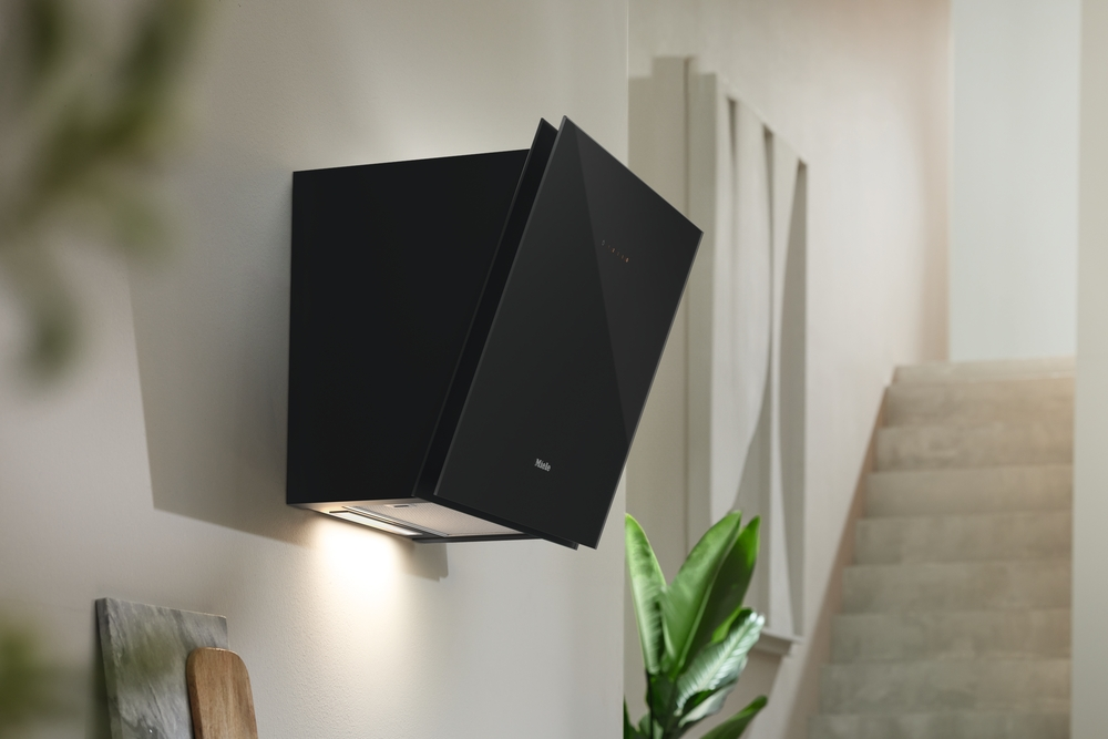 Eine schwarze Miele Dunstabzugshaube an einer hellen Wand montiert, mit Treppe im Hintergrund.