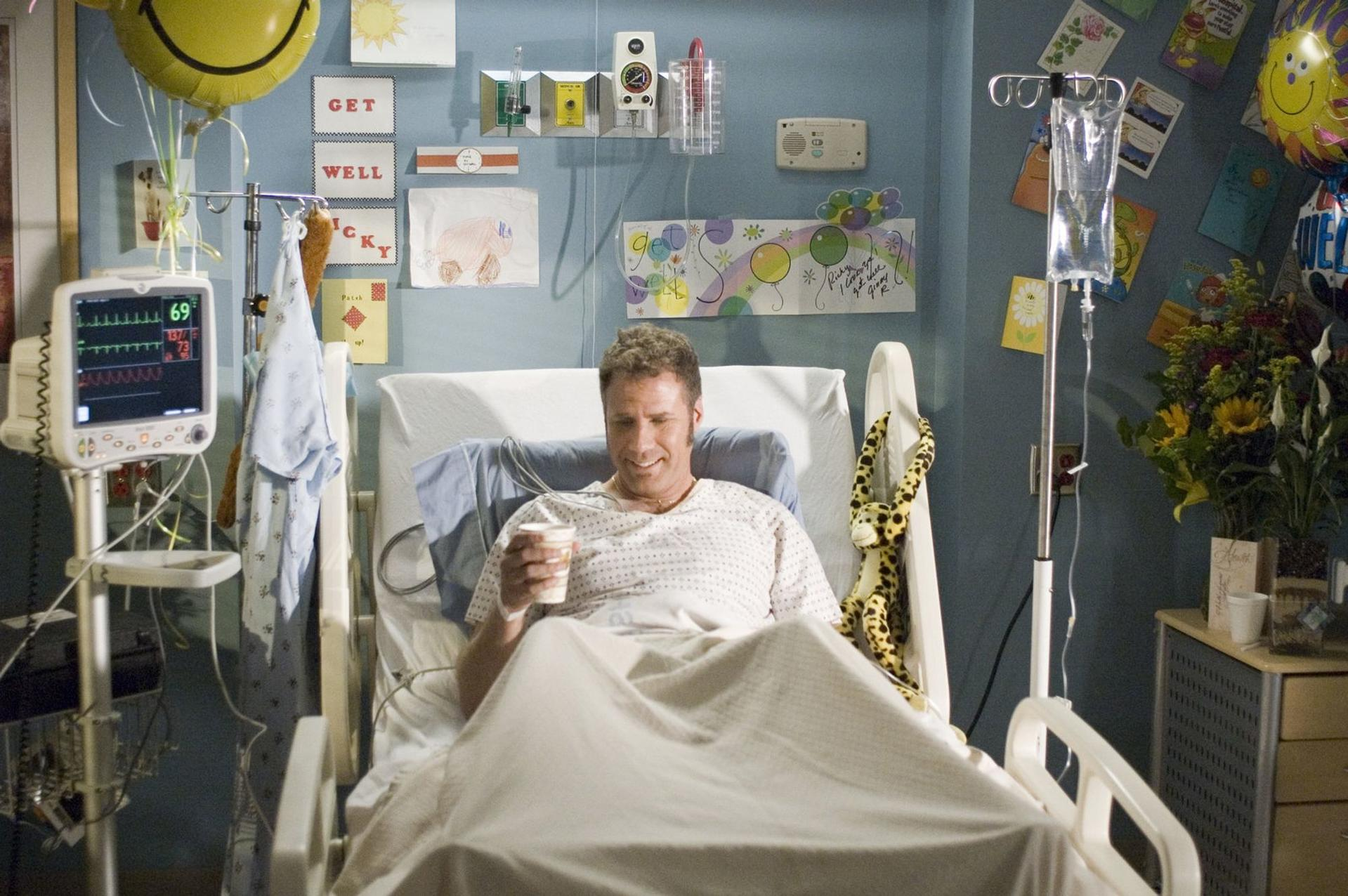 Ein Mann im Krankenhausbett trinkt aus einem Becher. Heilkarten schmücken die Wand.